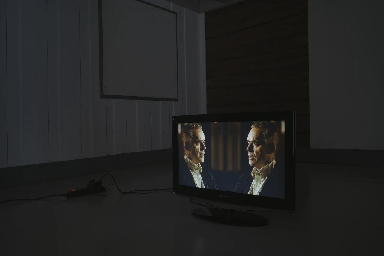 A television screen displaying Jordan Peterson in a conversation with himself in a mirror.