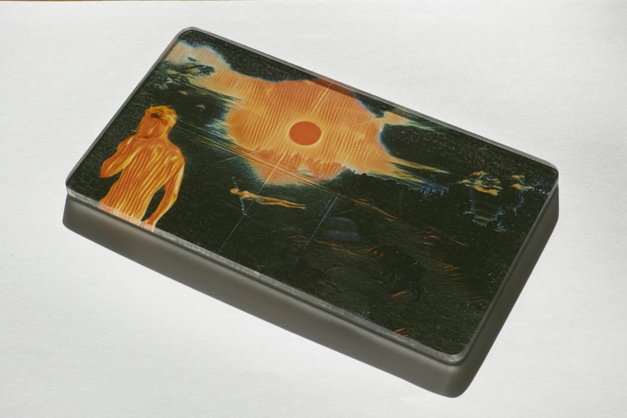 A rectangular object with a dark, artistic sunset scene on its surface, featuring a stylized human figure on the left and a bright sun in the sky.