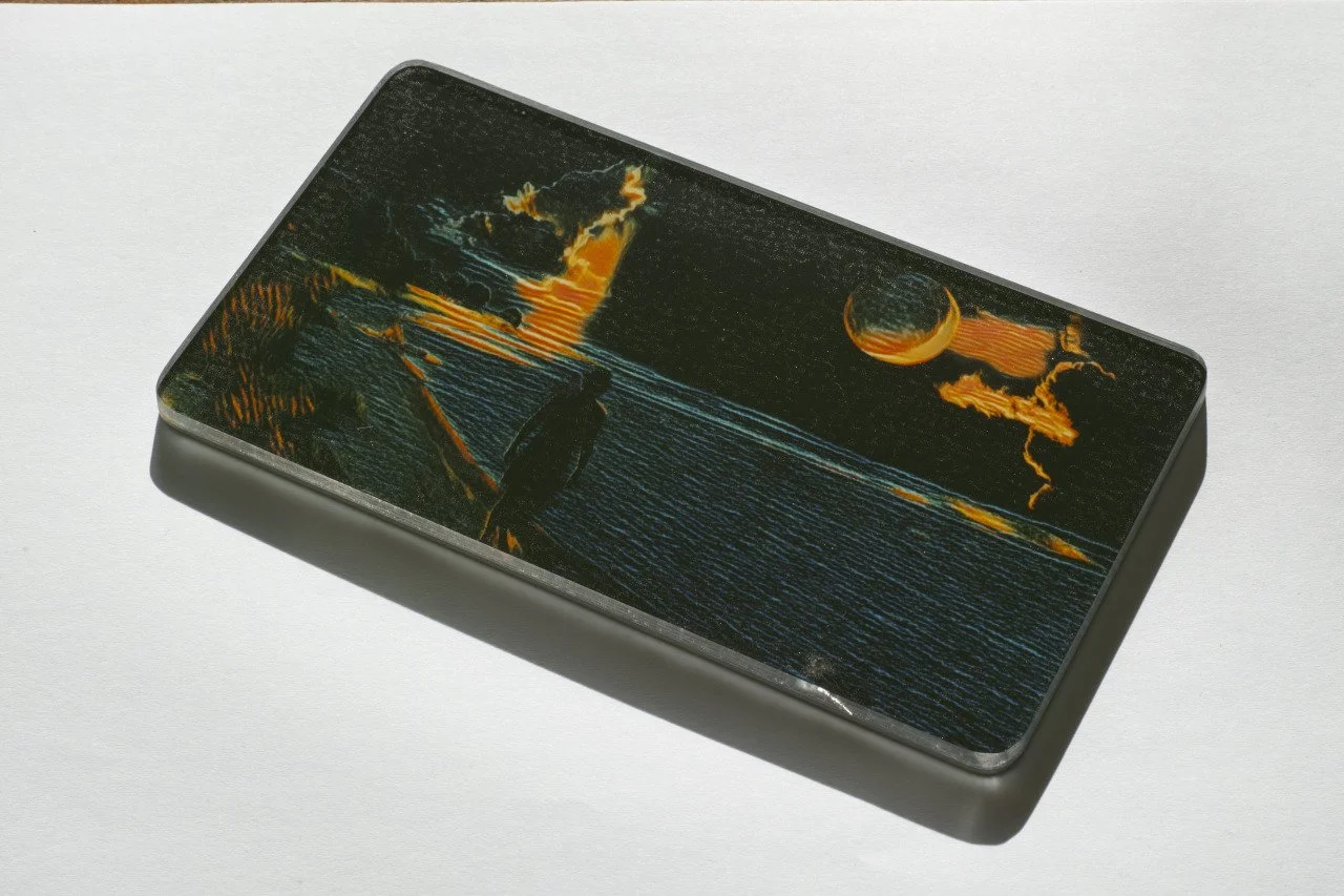 A rectangular device with a scenic beach sunset image on its screen, depicting a person walking along the shore, with the sun setting over the ocean.