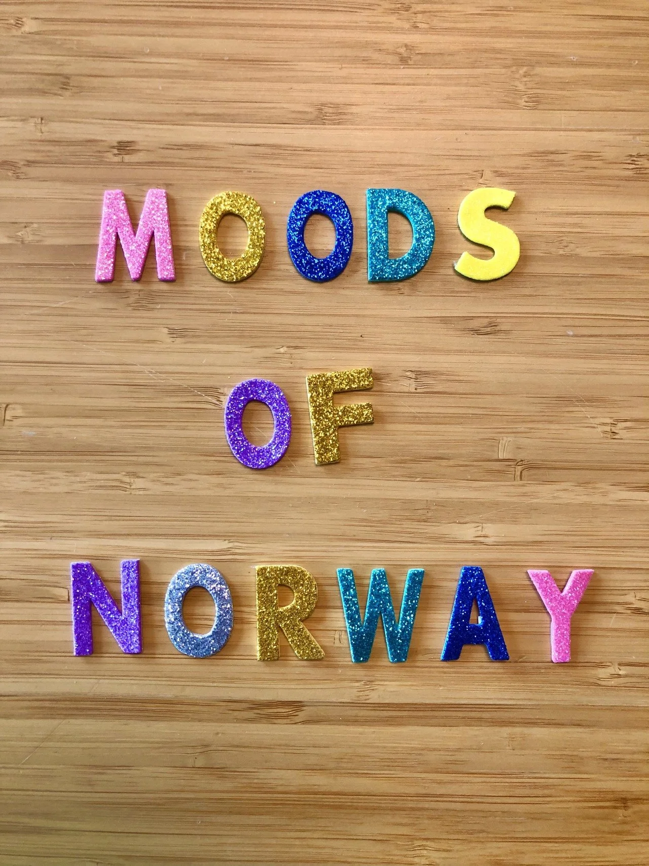 Colorful glitter letters spell out 'MODS OF NORWAY' on a wooden surface.