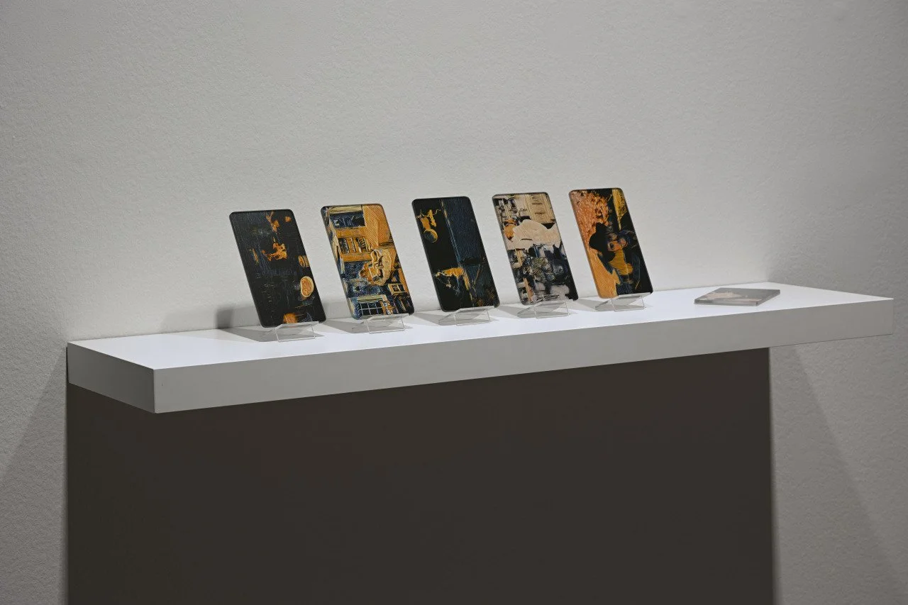 Five smartphones displayed on a white pedestal, showcasing different artwork or photographs, with one additional phone lying flat on the right.