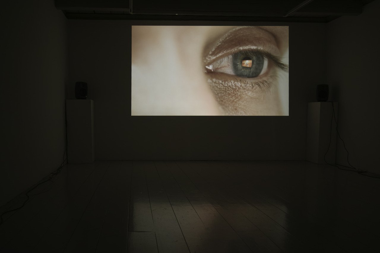 A large close-up image of a human eye projected on a dark wall in a gallery or room.
