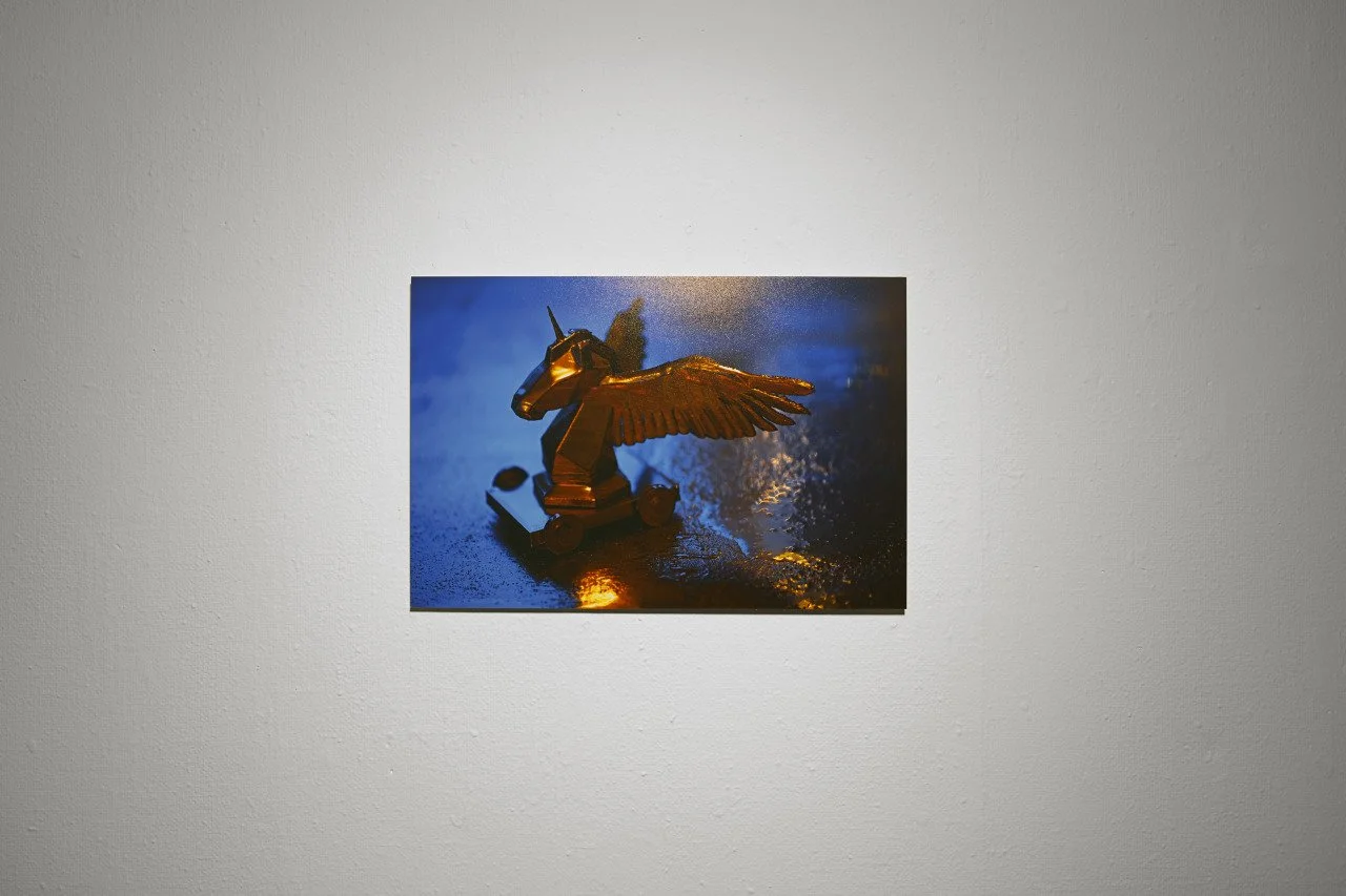 A photograph of a small, golden Trojan unicorn pegasus  with wings on a reflective surface, illuminated with colorful lighting.