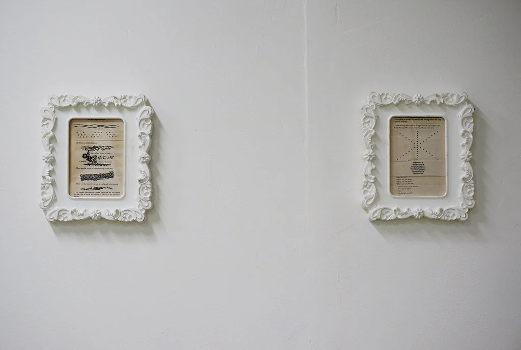Two framed pieces of paper with various graphics and text, mounted on a white wall.