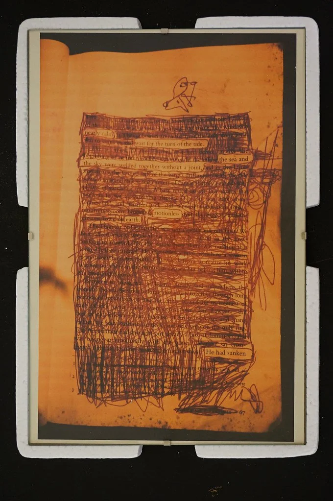 A page from a book with handwritten scribbles and a small drawing of a stick figure with glasses at the top. Text from the book is partially visible, including phrases like 'wait for the turn of the tide,' 'and the sea and the sky were welded togethe