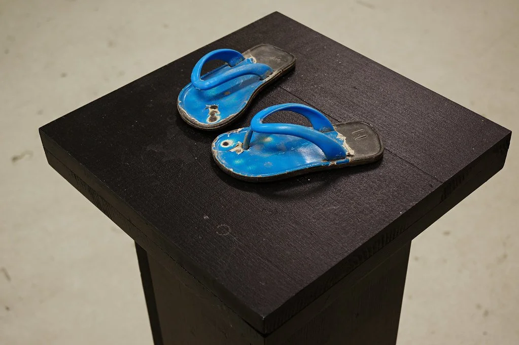 Pair of worn blue flip-flops on a black pedestal.