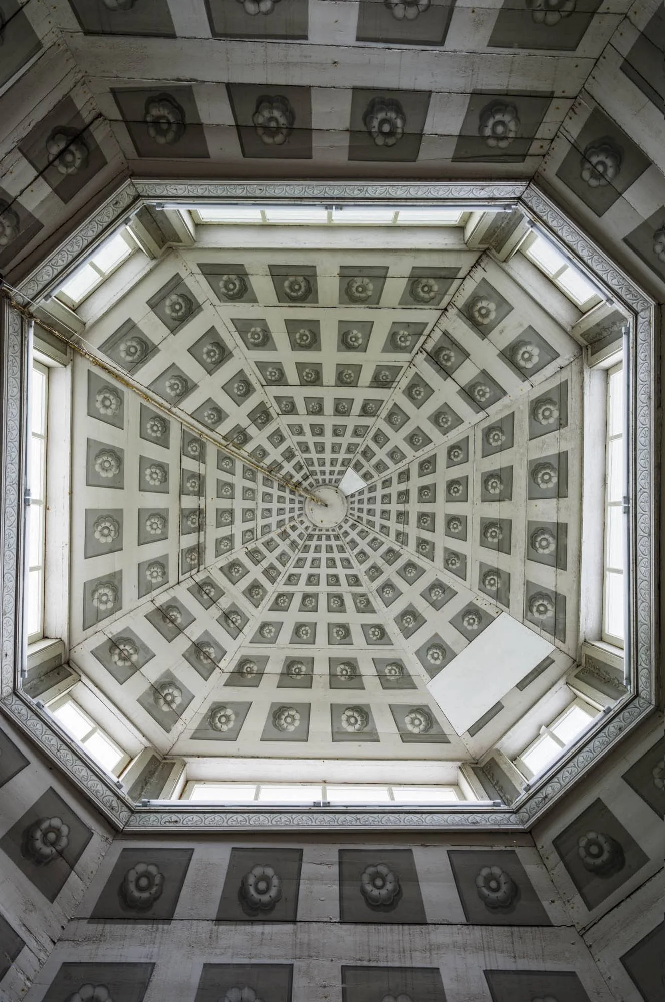 Interior view of a tall octagonal ceiling with patterned panels and windows around the edges, looking upward from the bottom inside a building.
