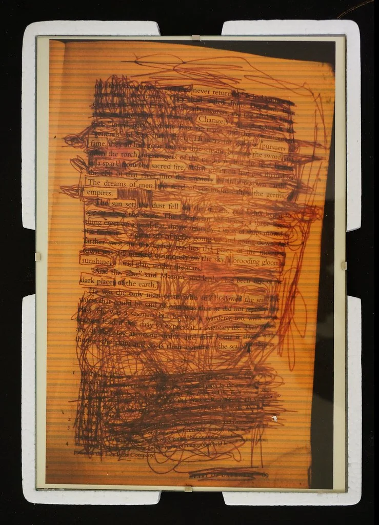 A tablet screen with a page of text that has been heavily scribbled over with black and orange ink, obscuring much of the original text.