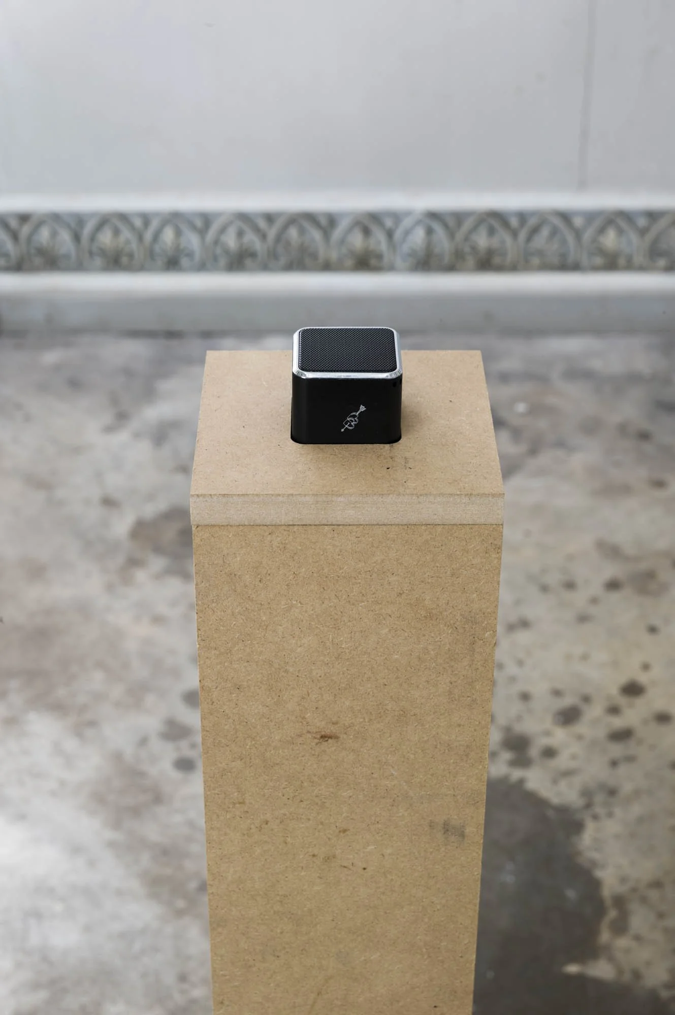 A black portable speaker placed on a rectangular wooden pedestal.