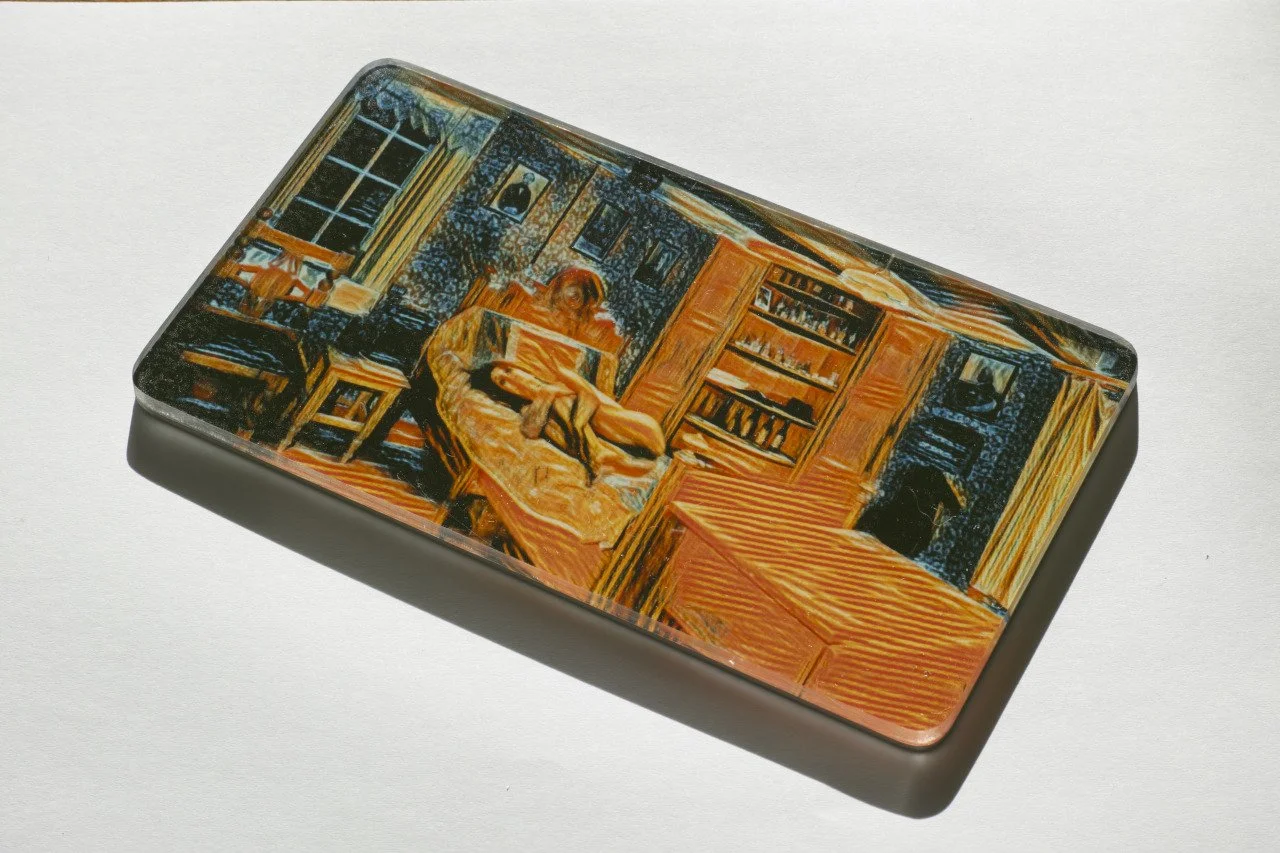 Close-up of a rectangular box with a colorful, abstract painting of a woman reading a book in a cozy room with bookshelves.