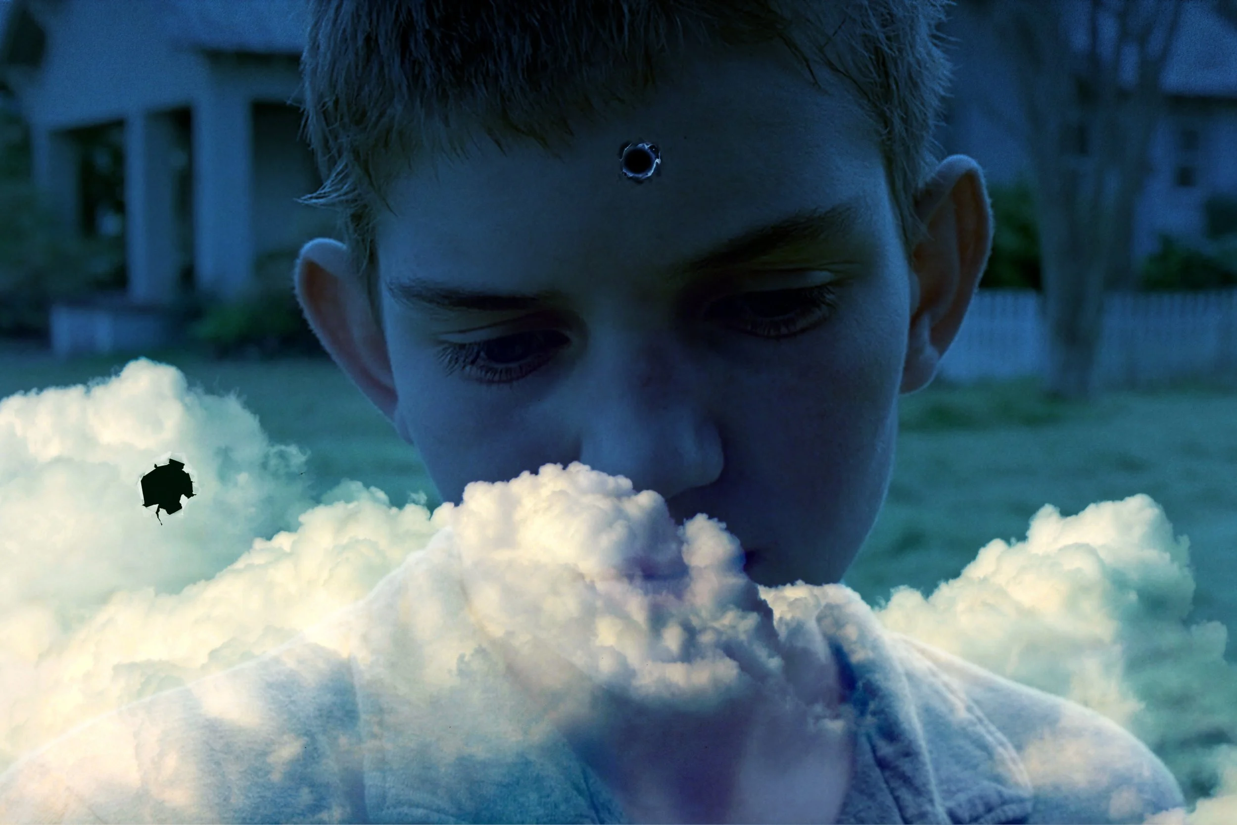 A boy with short hair looking downward with a serious expression, standing outdoors during dusk or early evening, with clouds and a solar eclipse visible in the sky.