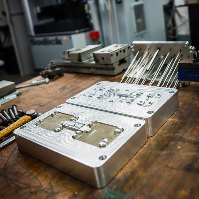 Metal mold with intricate carvings on a wooden workbench in a manufacturing workshop.