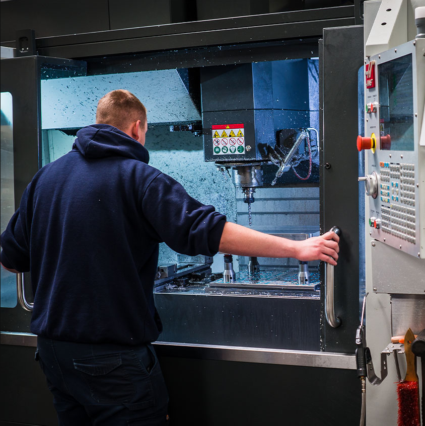 A person operating a CNC milling machine in a manufacturing facility.