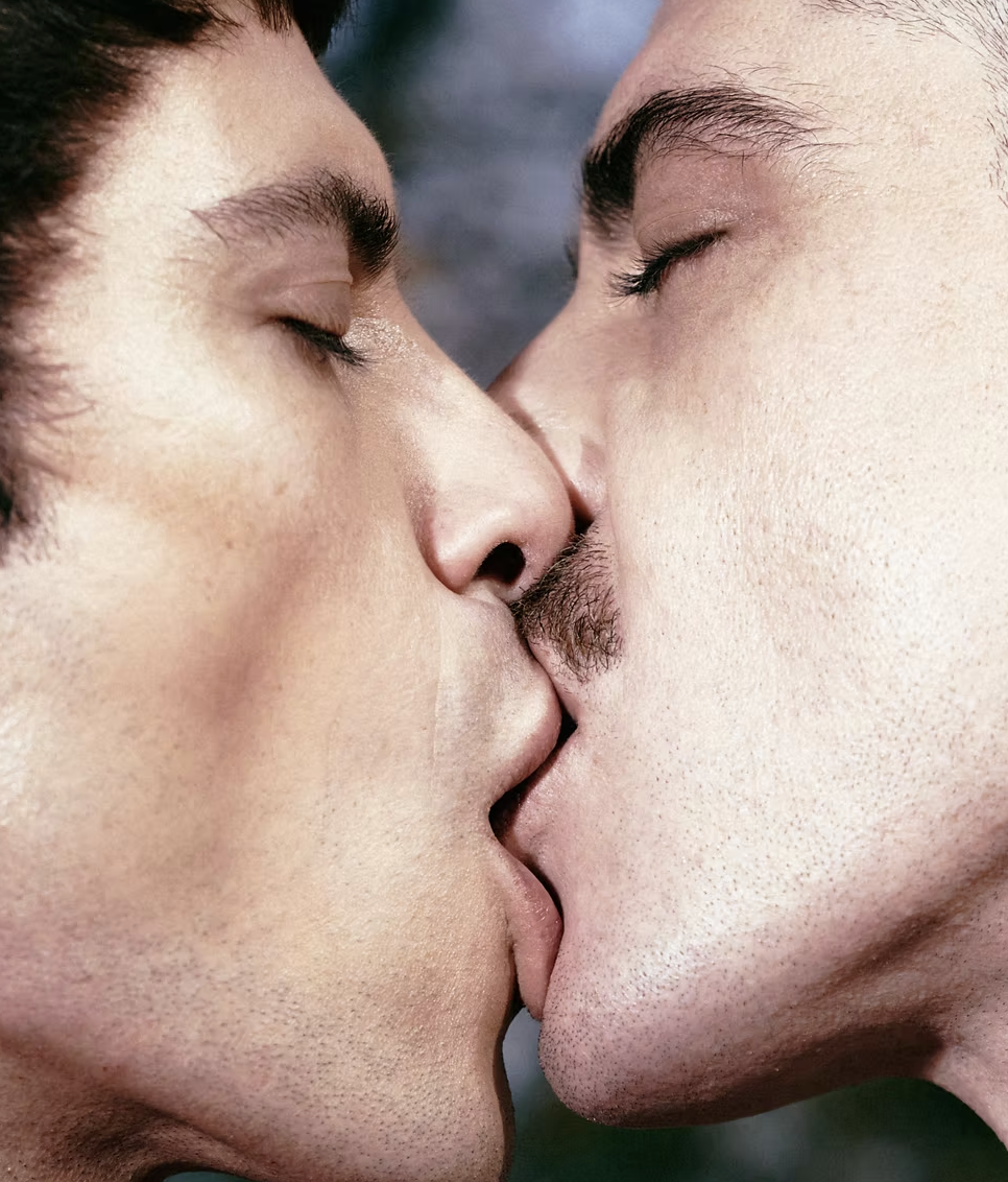 Two men with eyes closed, touching foreheads and kissing.