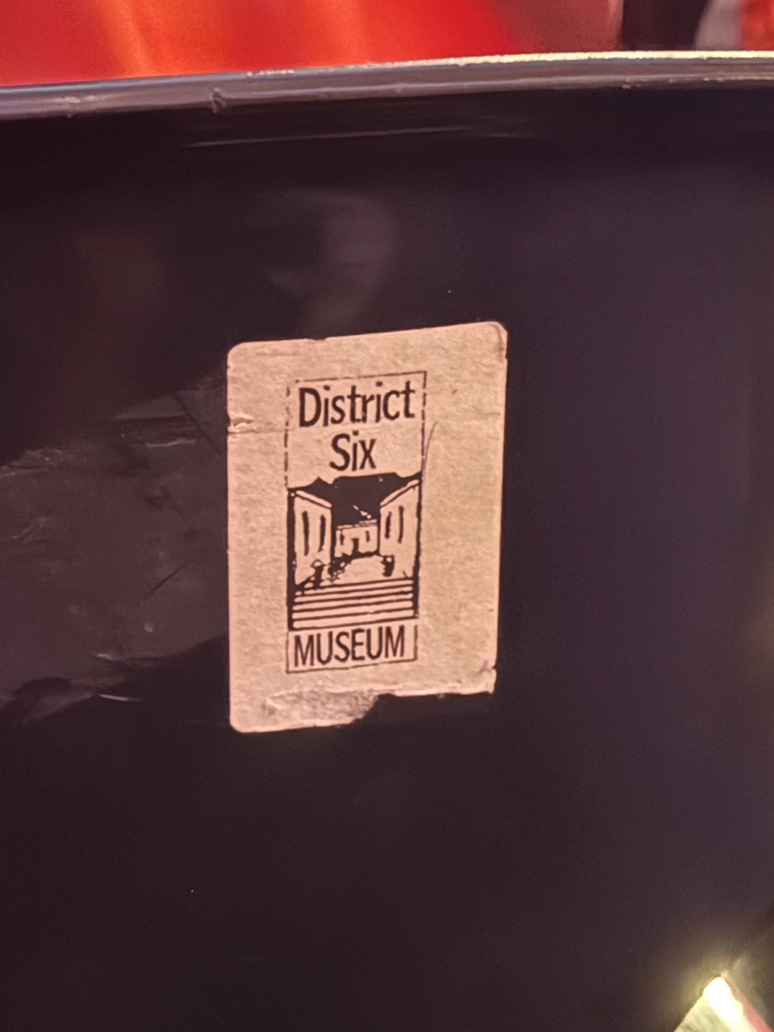 A sticker on a dark surface that says 'District Six Museum' with an illustration of a historic building.