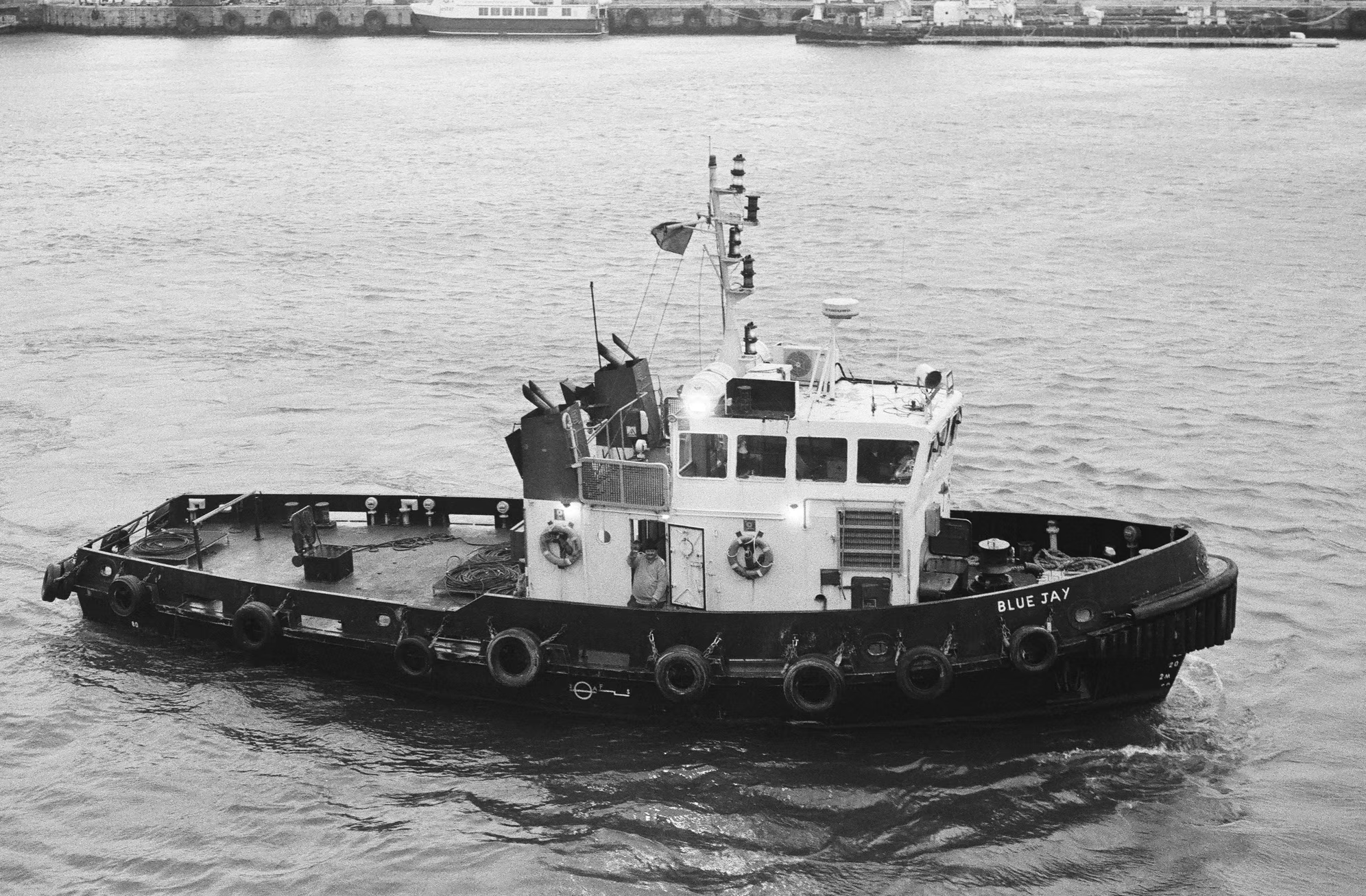 Black and white photo of tugboat named Blue Jay sailing on water.