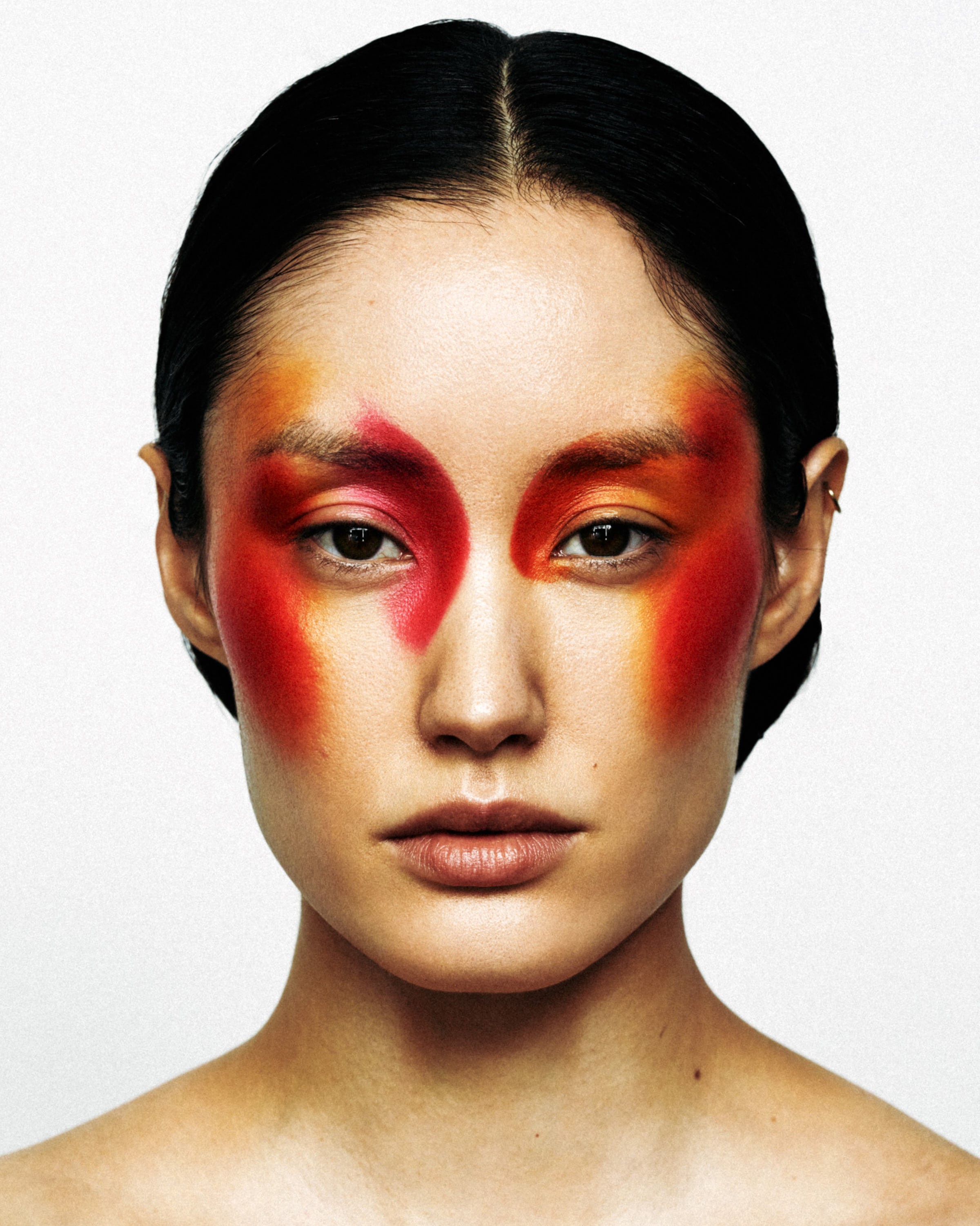 Close-up of a woman with vibrant red, orange, and yellow eye makeup blending across her face.