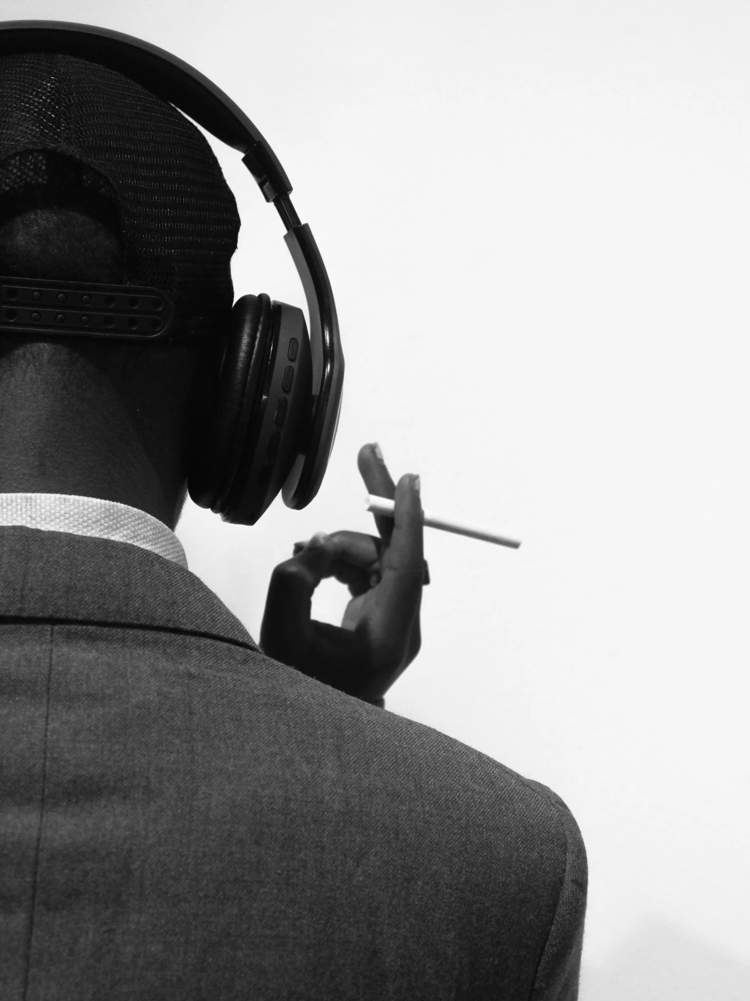 Person in a suit wearing headphones, smoking a cigarette, facing away from the camera against a plain white background.