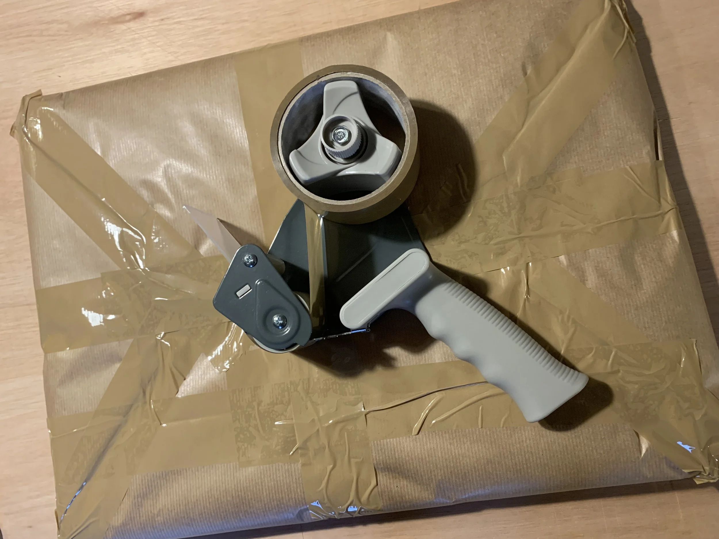 A tape dispenser with clear packing tape on a wooden surface.