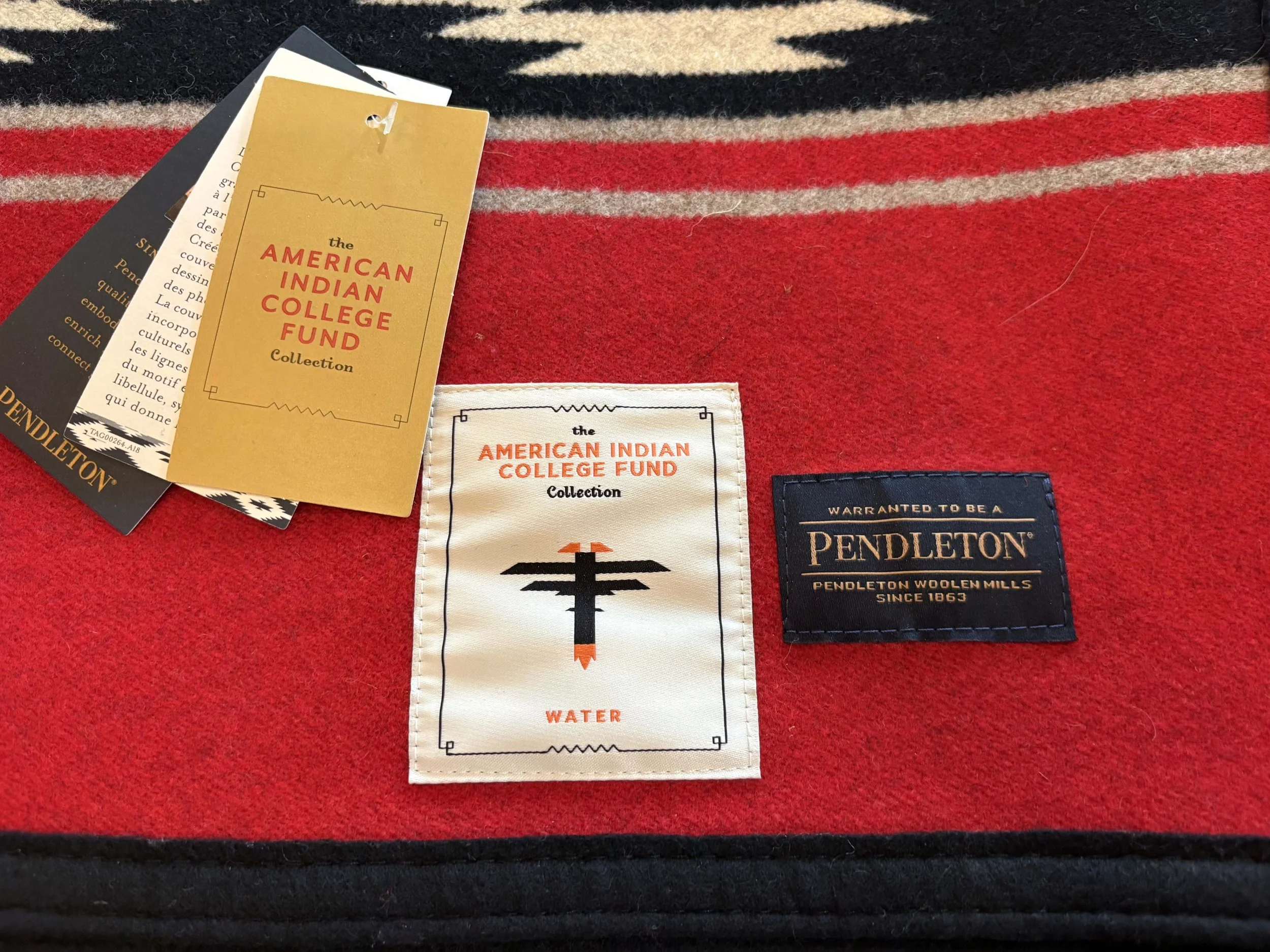 Close-up of clothing tags on a red fabric, including one for Pendleton Woolen Mills and others for American Indian College Fund and water.