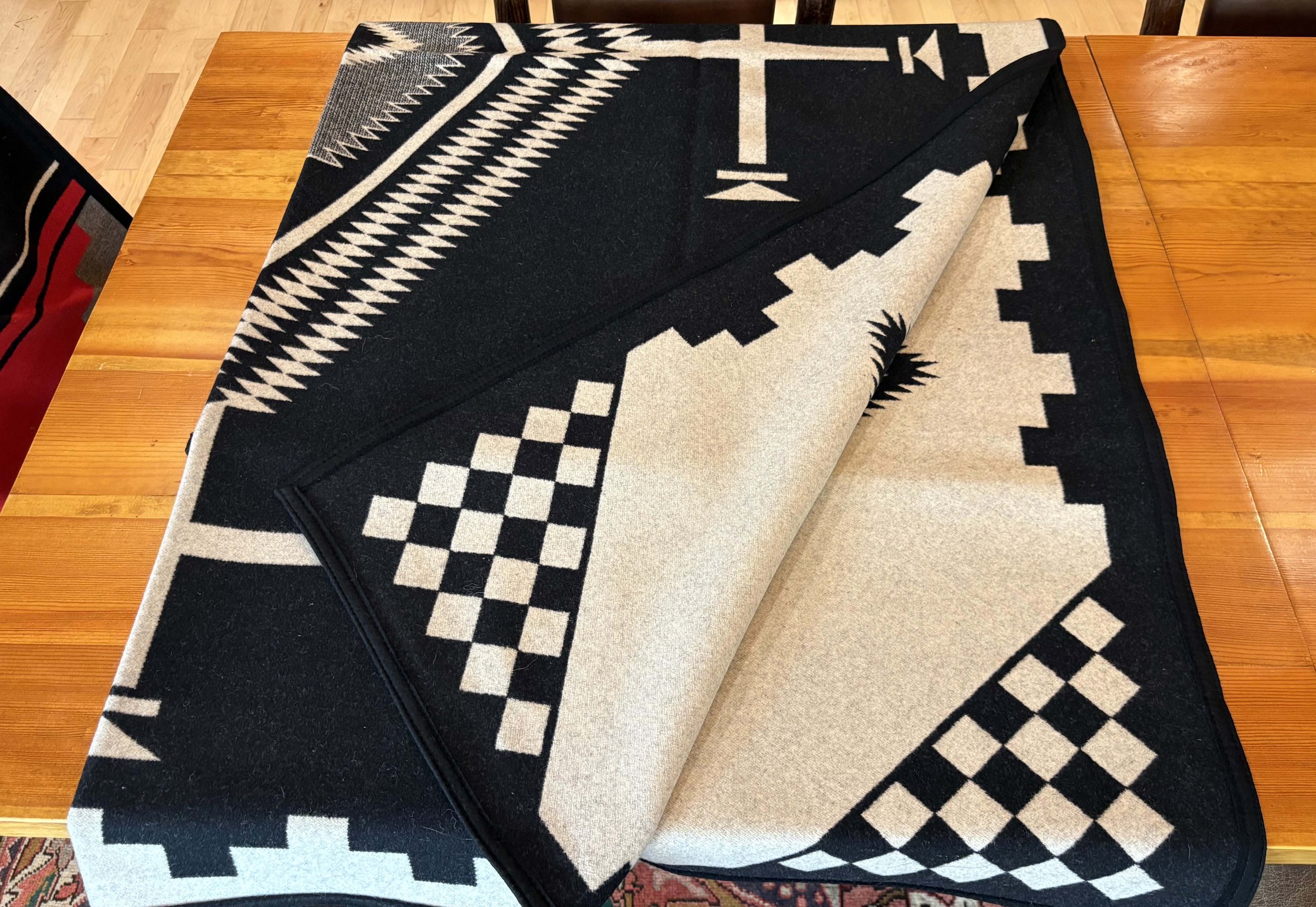 A patterned black and beige rug with geometric designs is partially rolled up on a wooden table.