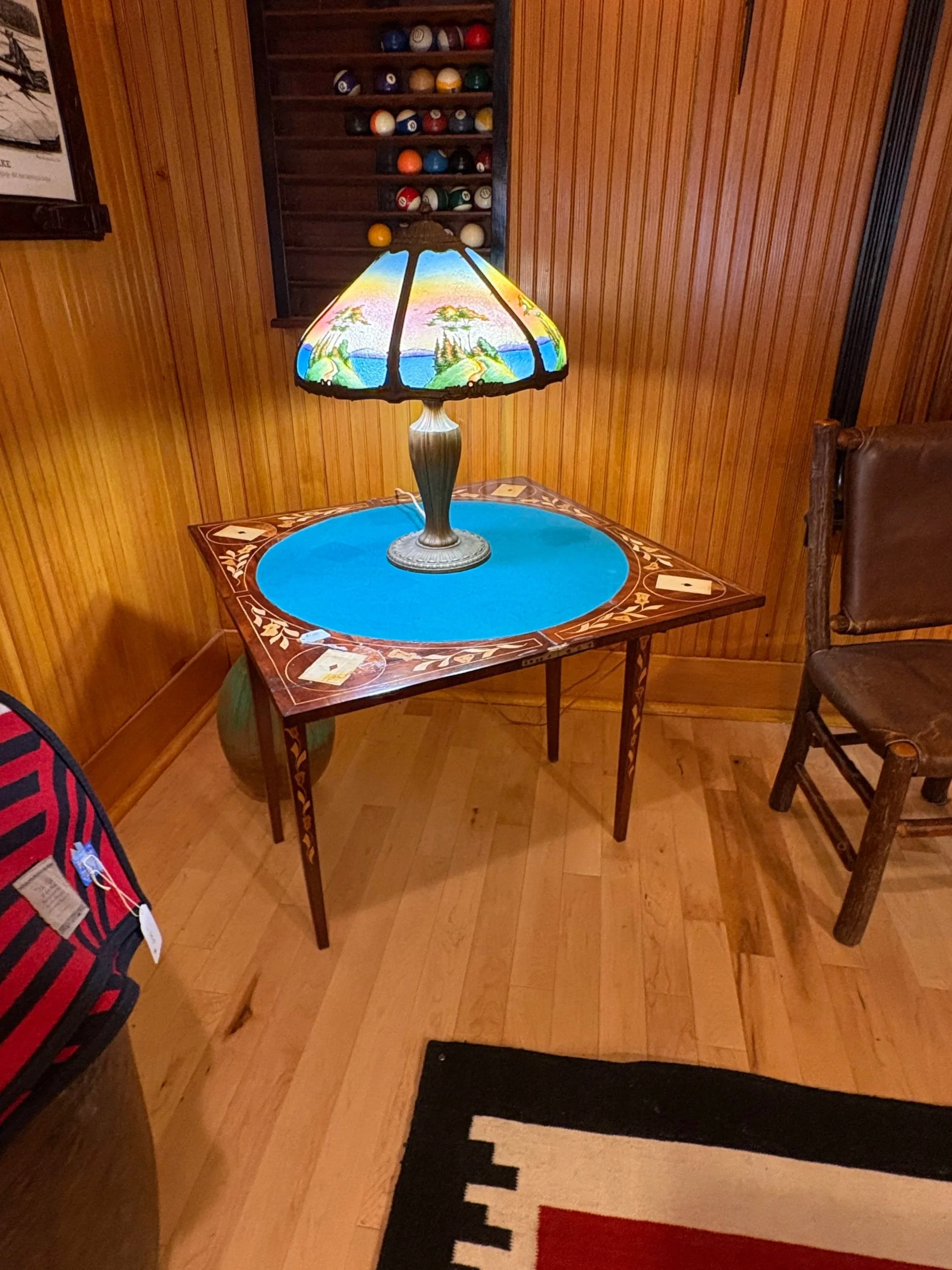 A cozy game room with wooden walls and ceiling, featuring a pool table in the center, traditional patterned area rugs, and various decorative items and windows providing natural light.