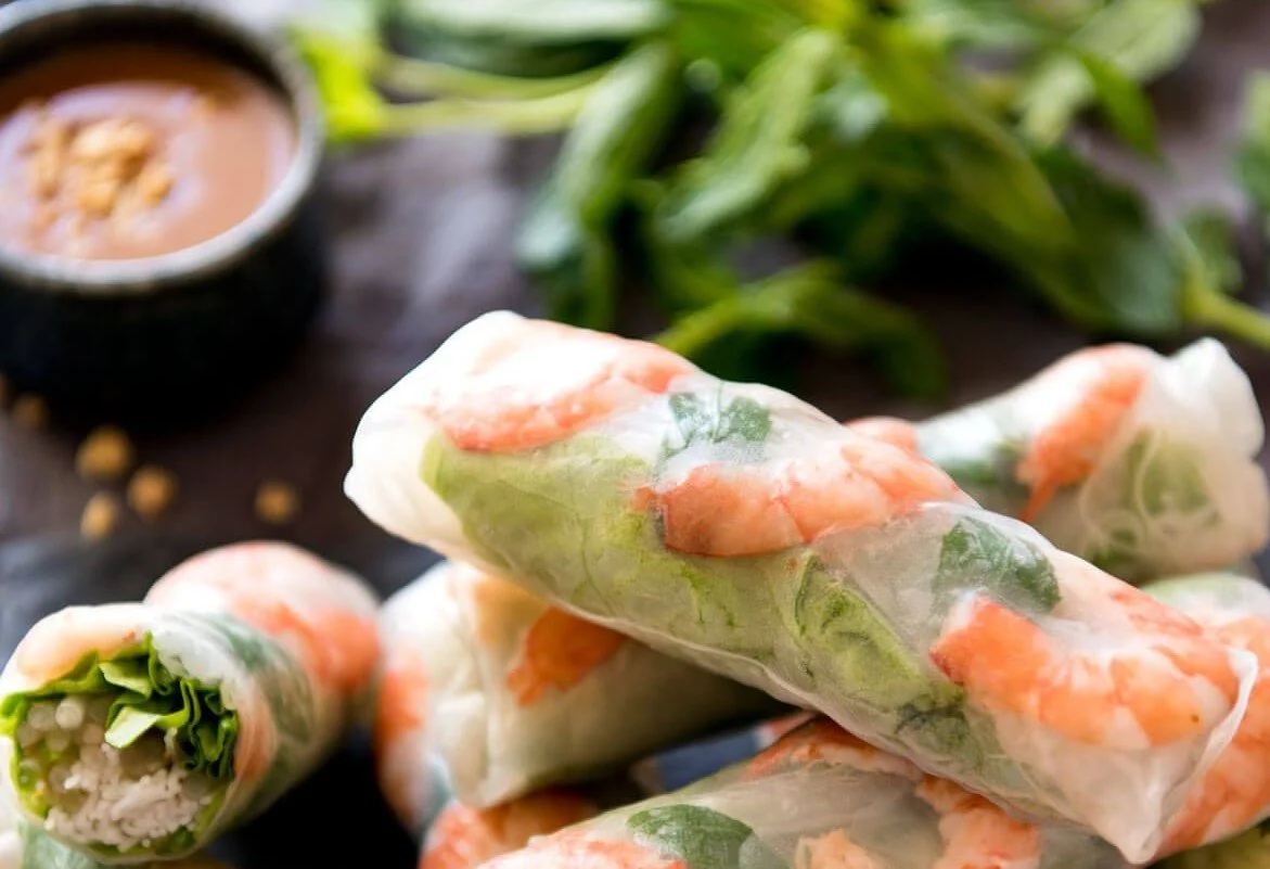 Spring rolls filled with shrimp, greens, and rice noodles, with a dipping sauce in the background.