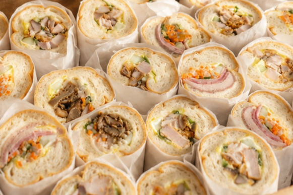 Assorted sandwiches with various fillings like chicken, ham, and vegetables, wrapped in white paper