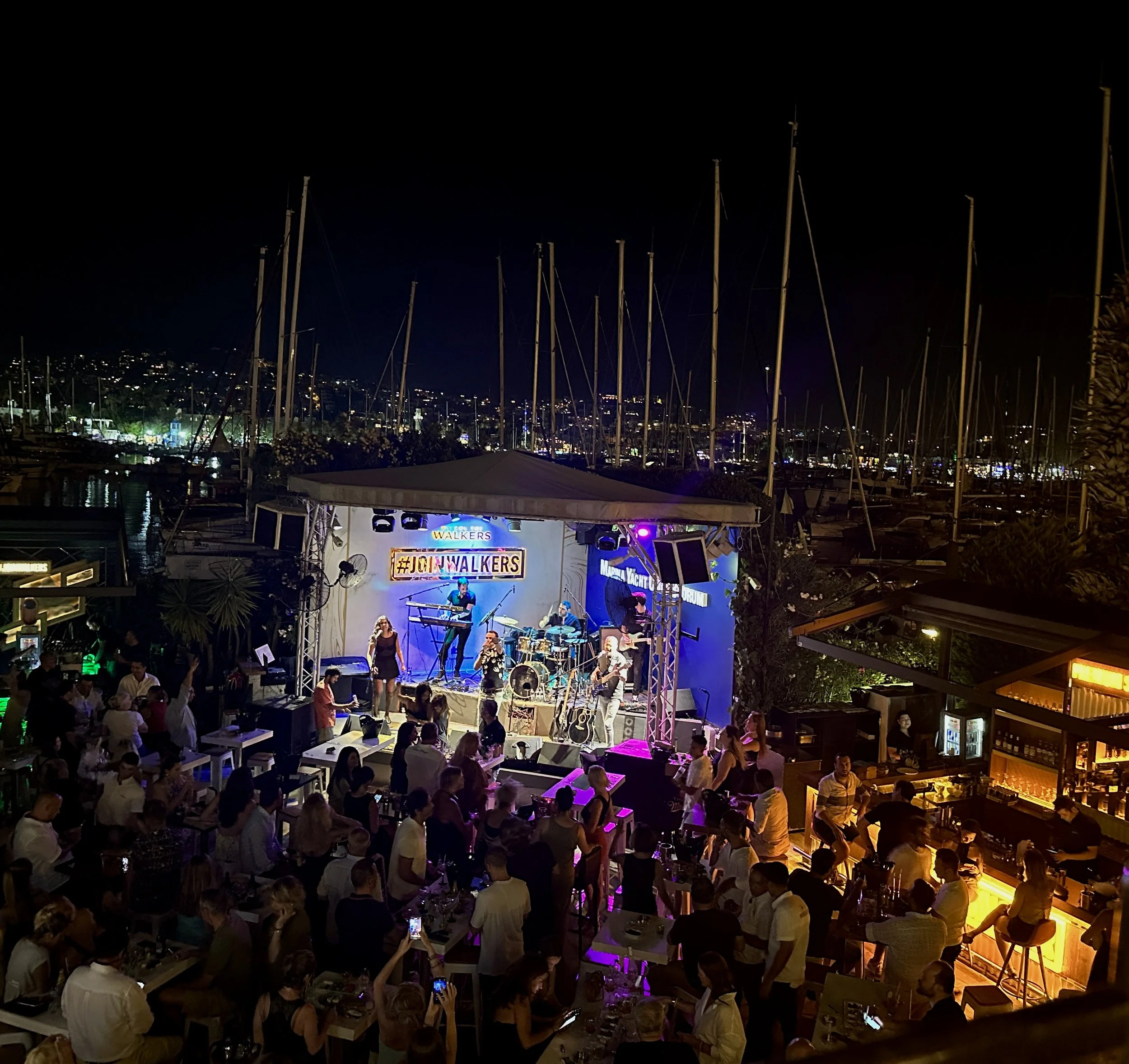 Luxury beach club in Bodrum with stylish sun loungers, turquoise Aegean waters, waterfront dining, live DJ atmosphere and yachts anchored just offshore.