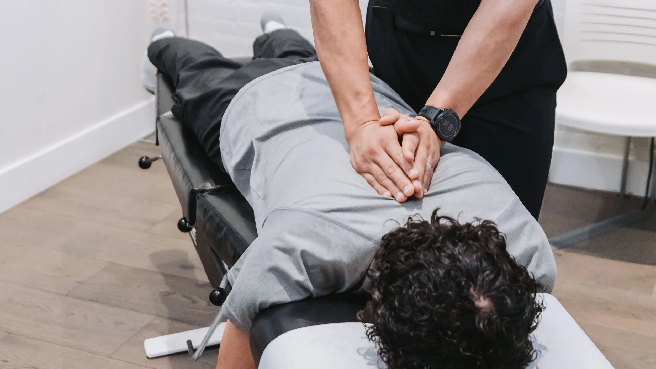 Chiropractor performing spinal adjustment on a patient lying face down on a chiropractic table in an office setting.