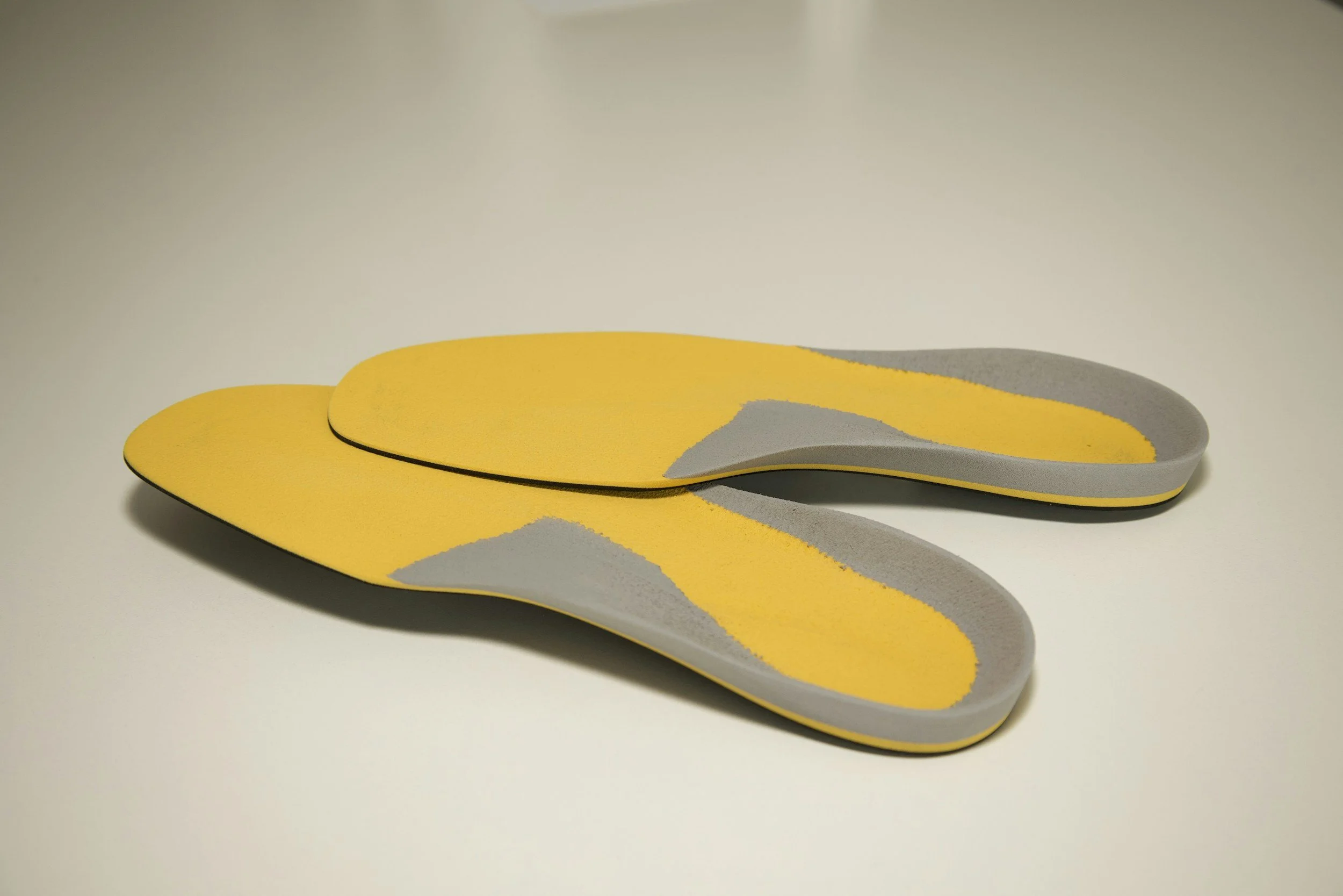 A pair of yellow and gray foam insoles placed on a white surface.
