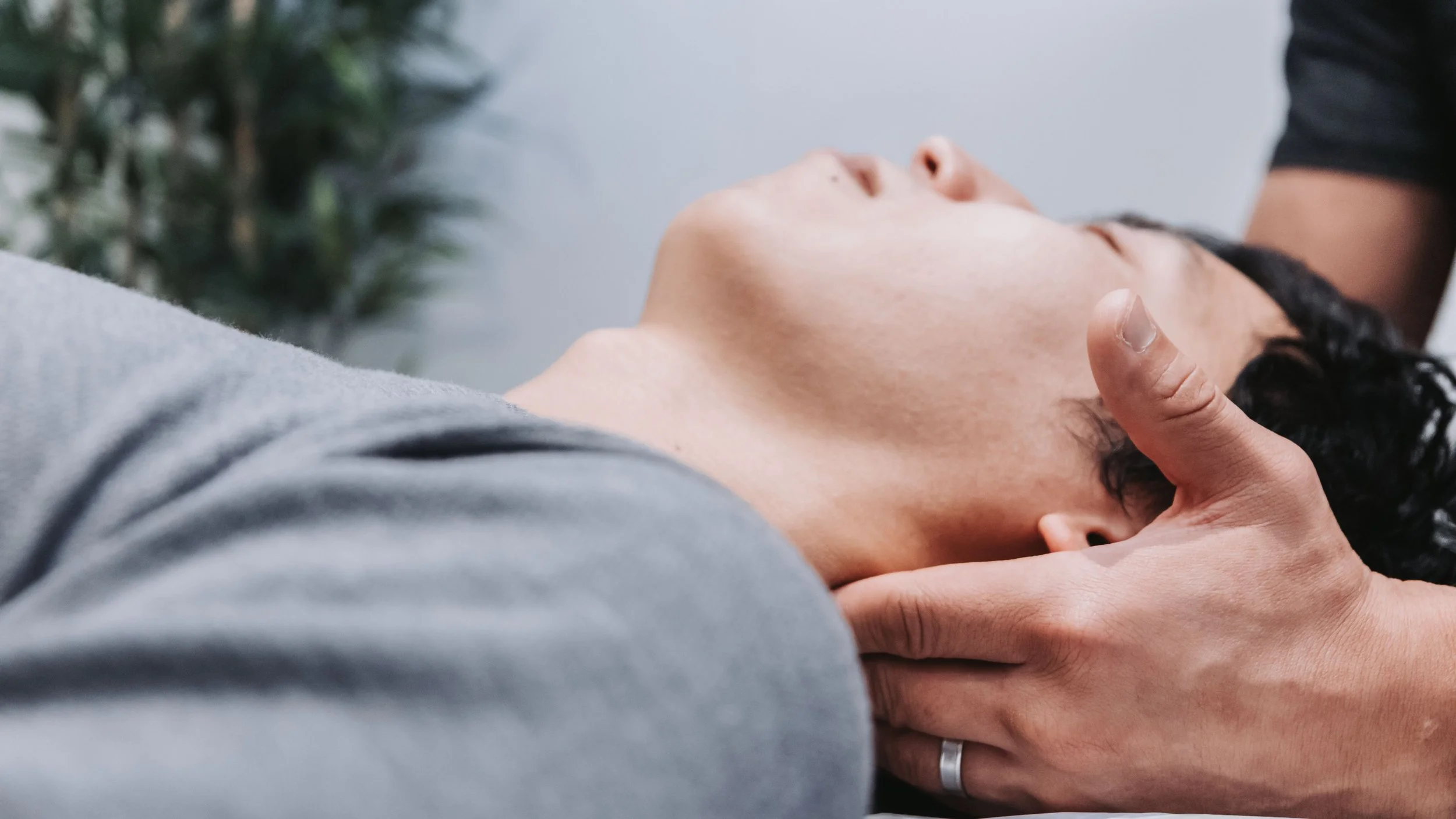 A person receiving a head massage, lying on their back with eyes closed, while another person uses their hands to massage their head.