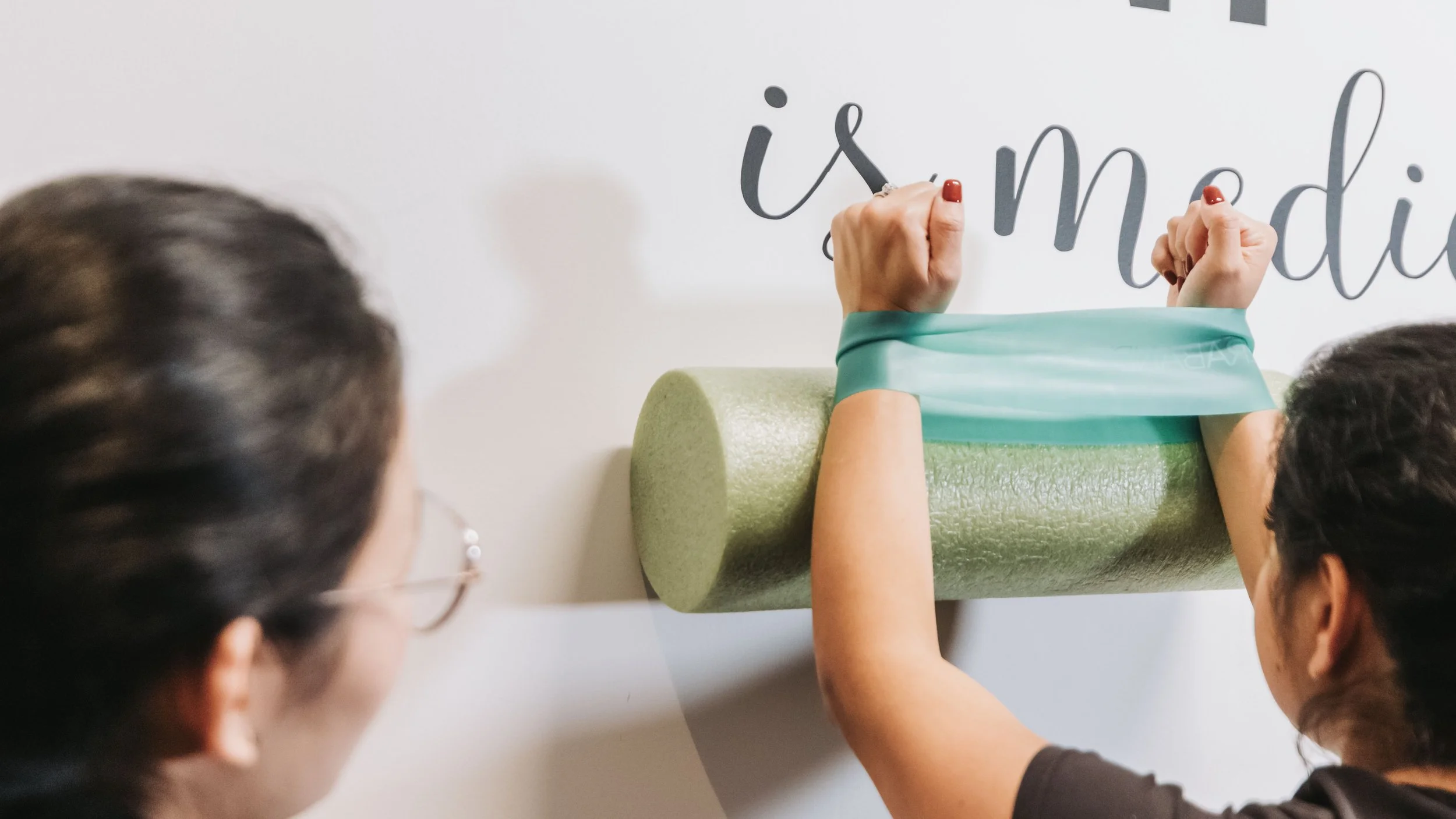 Two women are discussing typography on a wall, with one woman using her hands to arrange a phrase, and the other woman observing nearby.