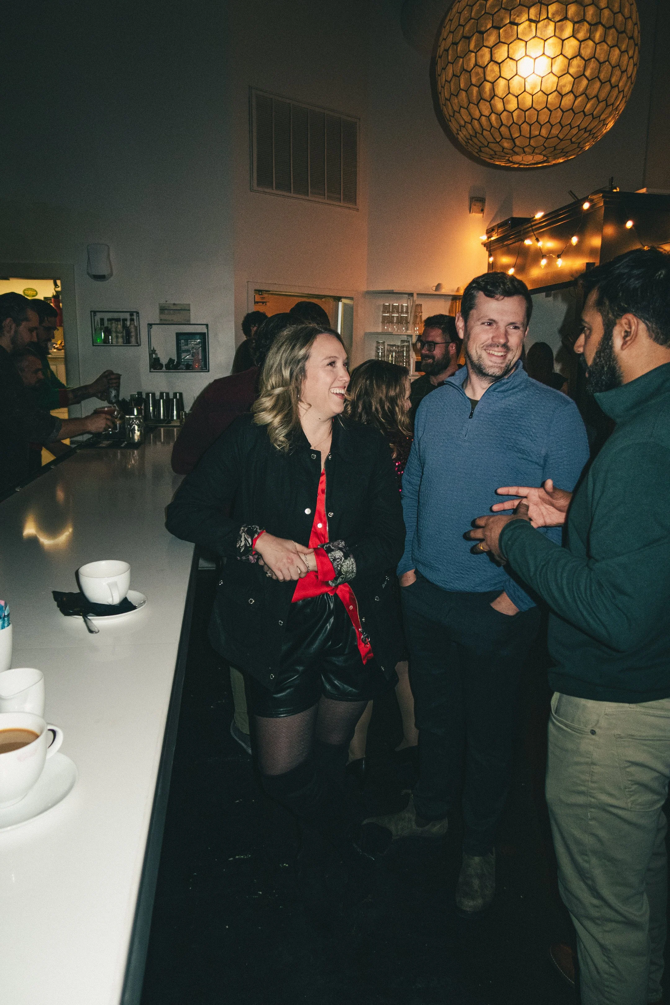 People socializing and chatting in a dimly lit bar or lounge with string lights and a decorative hanging light fixture.