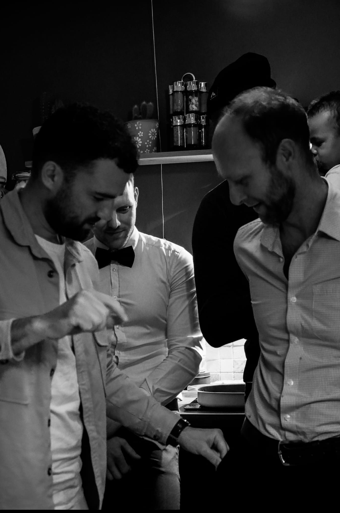 Groupe de personnes habillées formellement, discutant ou observant quelque chose ensemble dans une cuisine.