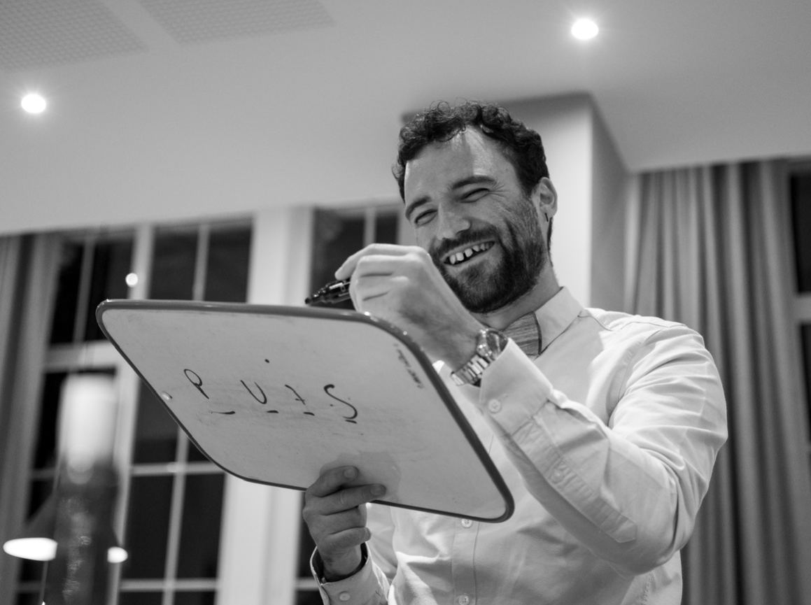 Homme souriant tenant un tableau blanc avec des écrits, en intérieur, en noir et blanc.