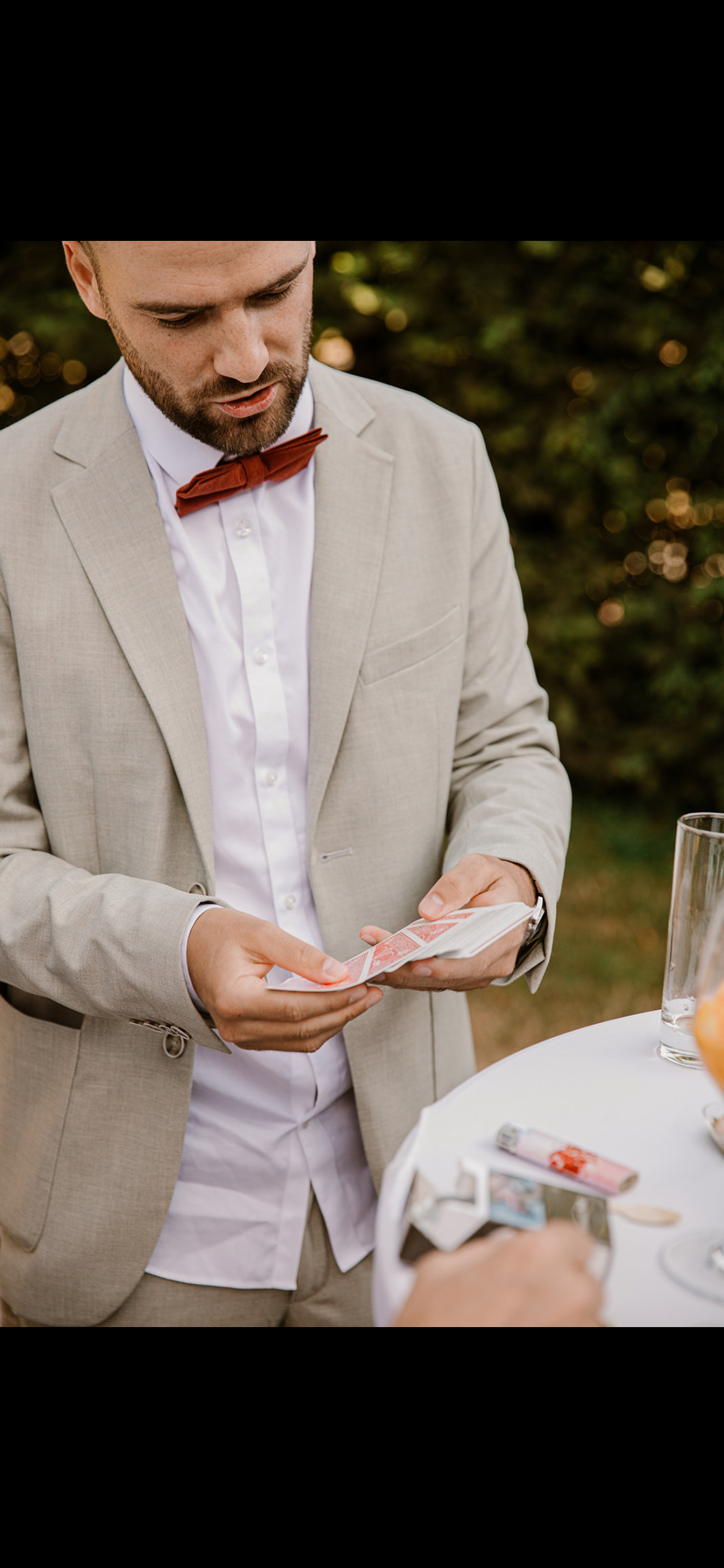 Un homme en costume clair et cravate marron joue aux cartes lors d'un événement en plein air.