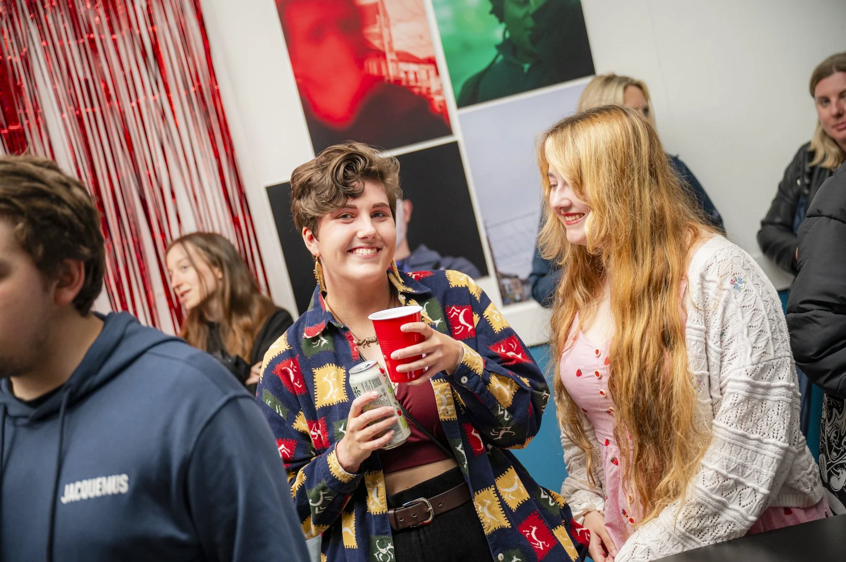 2 young people in crowded room smiling and holding drinks