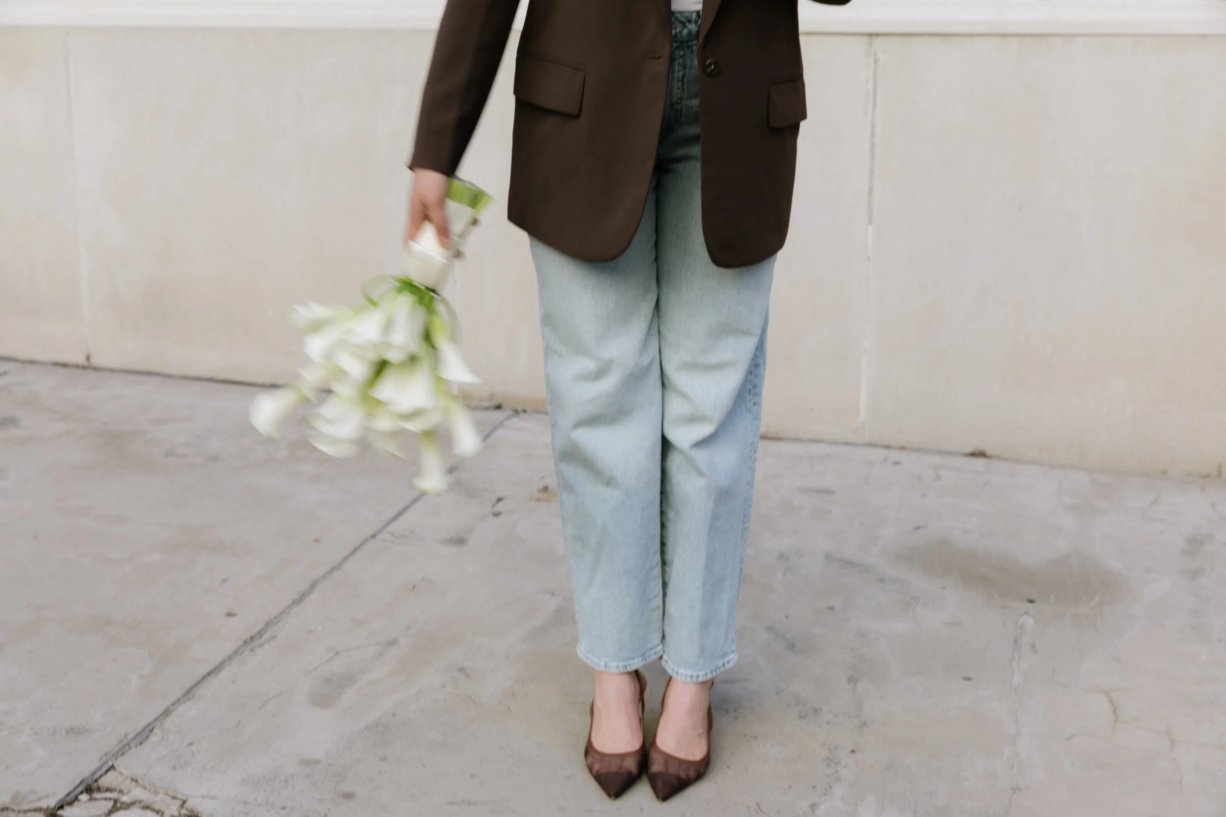 Person holding white calla lilies while standing in tailored attire