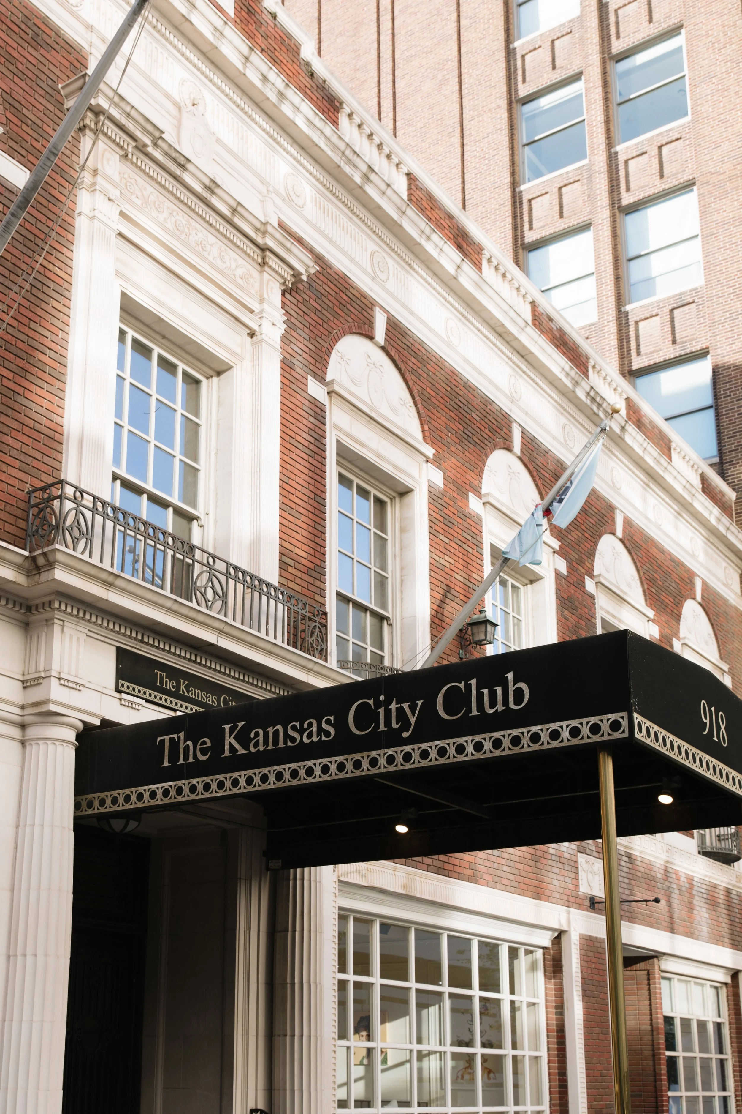The exterior brick facade of The Kansas City Club, featuring a black fabric awning over the entrance with the venue name in gold lettering.