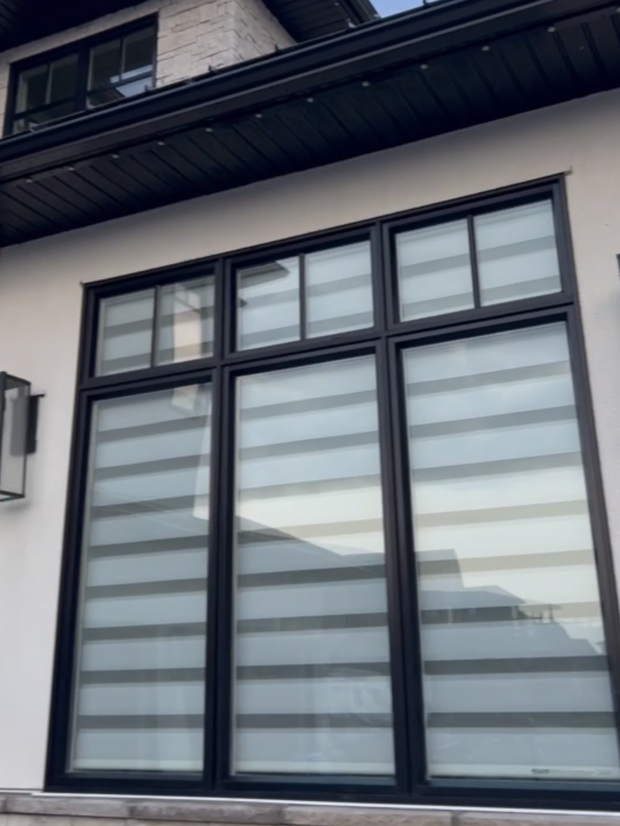 Close-up view of large, modern window with black metal frames on a beige and stone exterior wall of a building.