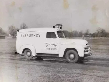 Black and white photo of an emergency vehicle from the Sulford Fire Department, labeled as an ambulance or rescue truck, parked on a paved road with trees in the background.