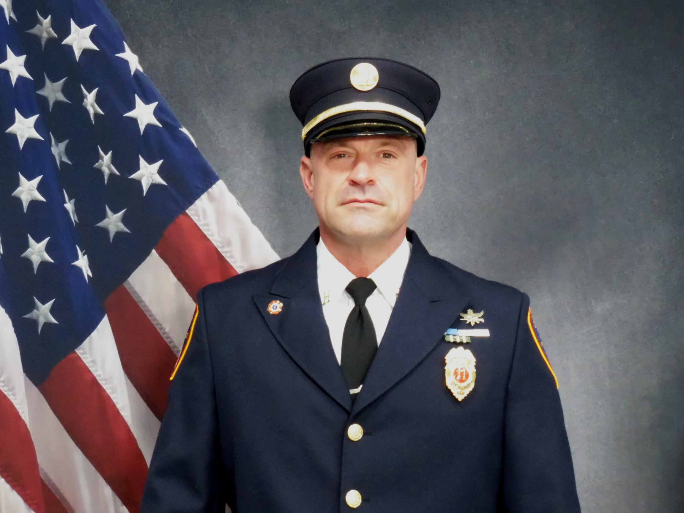 A man in a police uniform standing in front of the American flag.