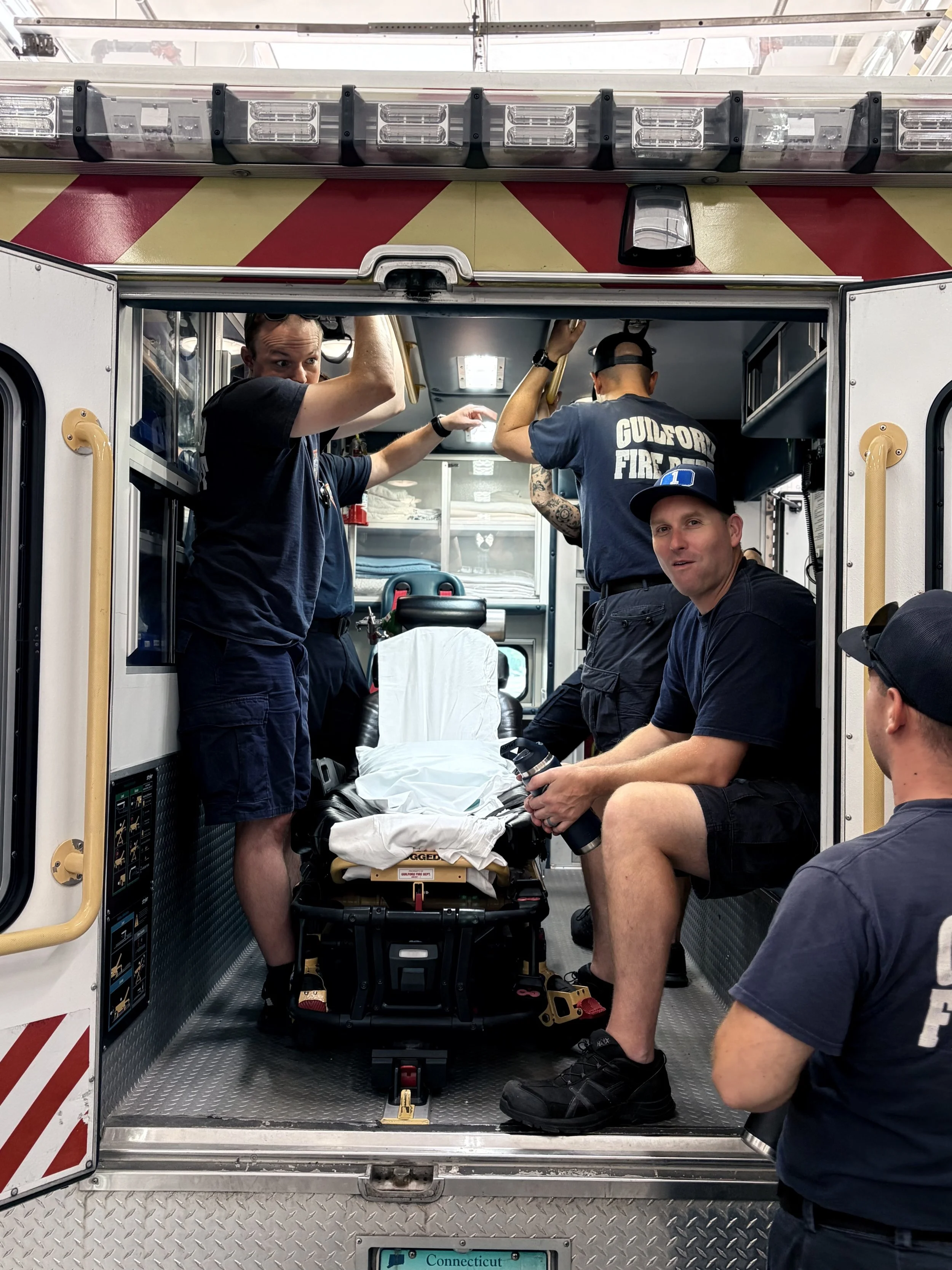 Firefighters inside an ambulance preparing a stretcher with a patient. The ambulance has a Connecticut license plate.