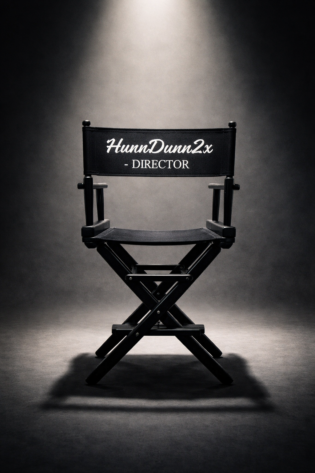 Director's chair with black fabric and white text reading 'HunnDunn2x - DIRECTOR' against a dark, spotlighted background.