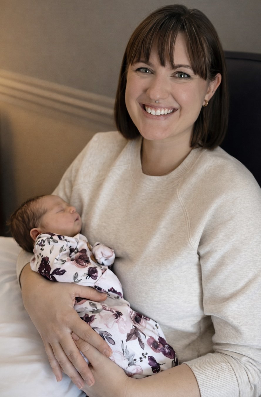 A smiling woman holding a sleeping newborn baby in her arm.