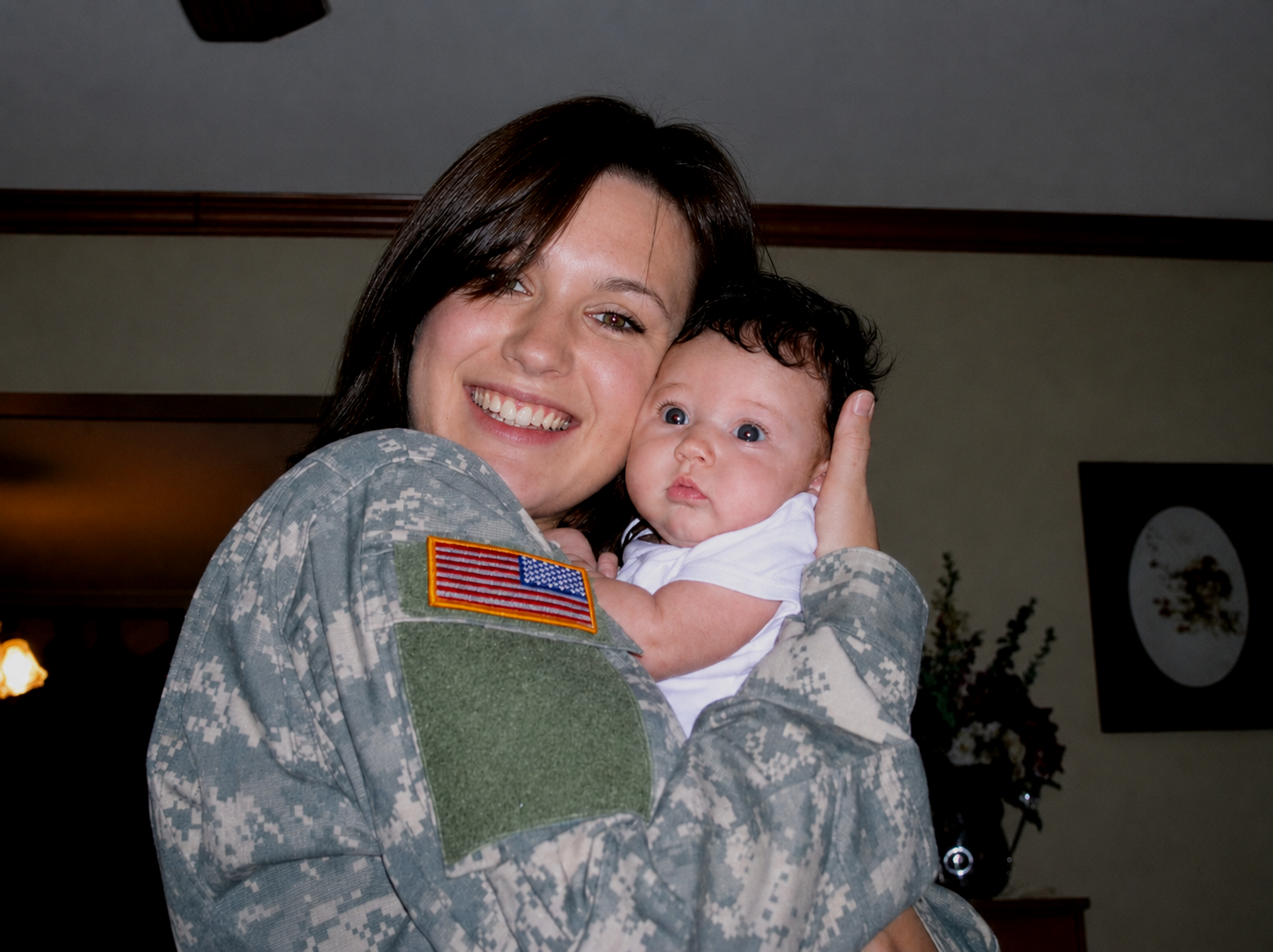 A woman in military uniform holding a baby in her arms and smiling.