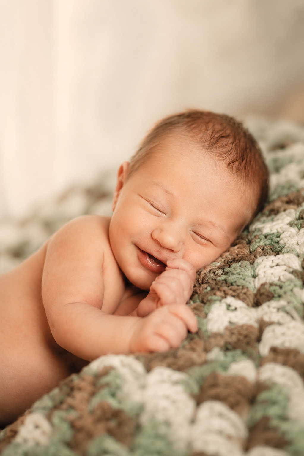 A smiling newborn baby lying on a multicolored crocheted blanket.