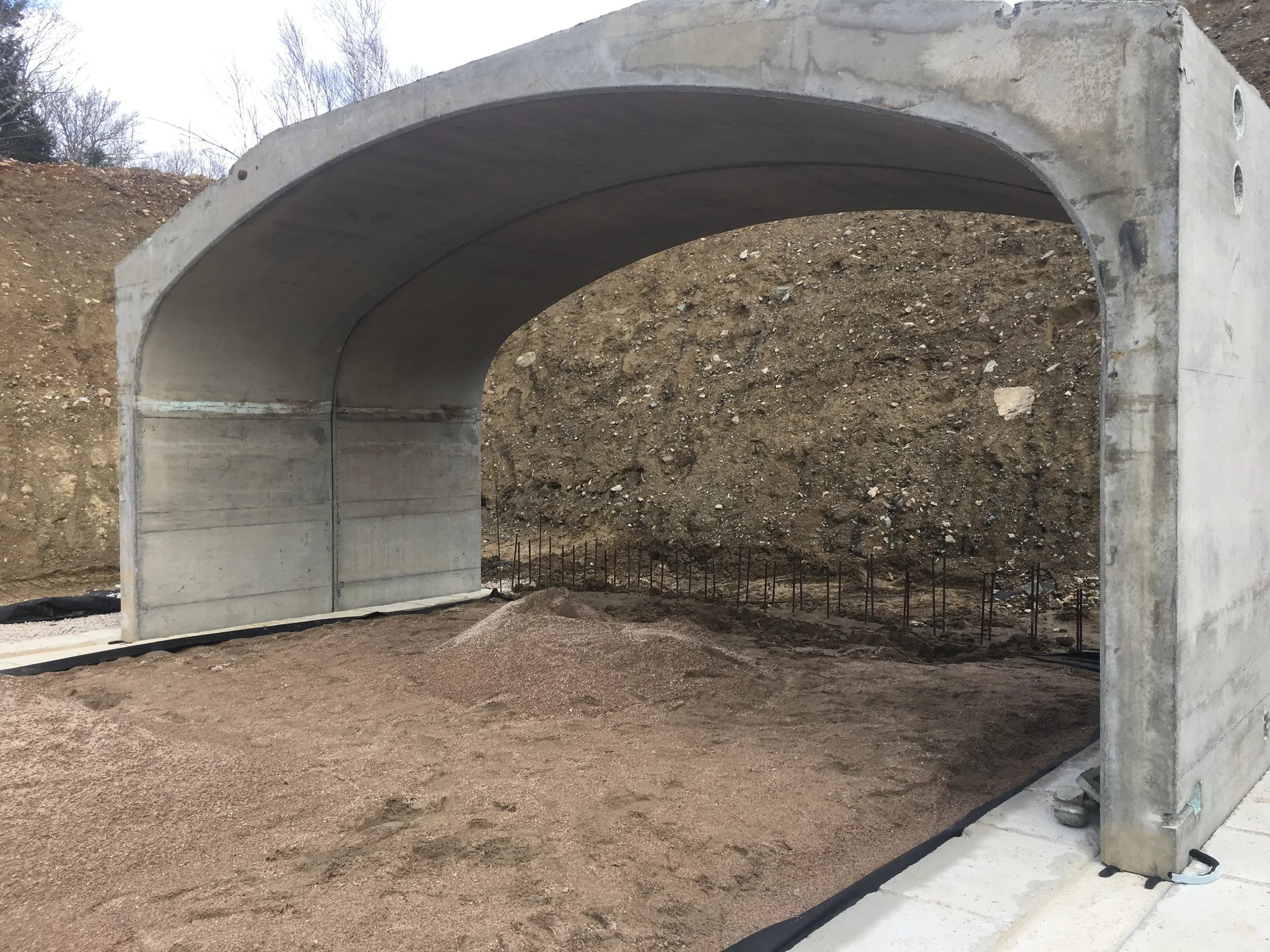 Concrete tunnel under construction with soil and rebar in the background.