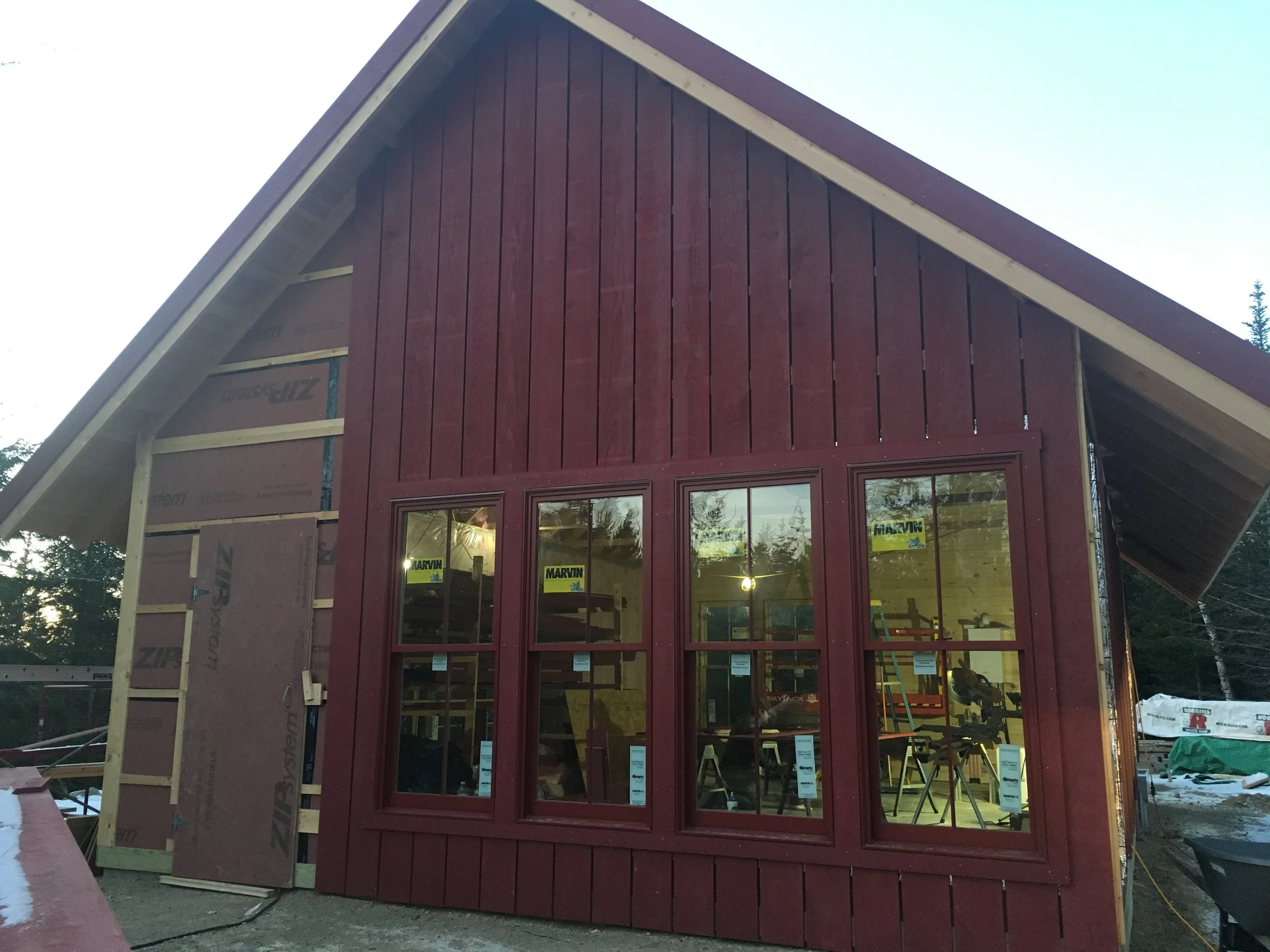 A house under construction with red siding and large windows, showing interior tools and work area.